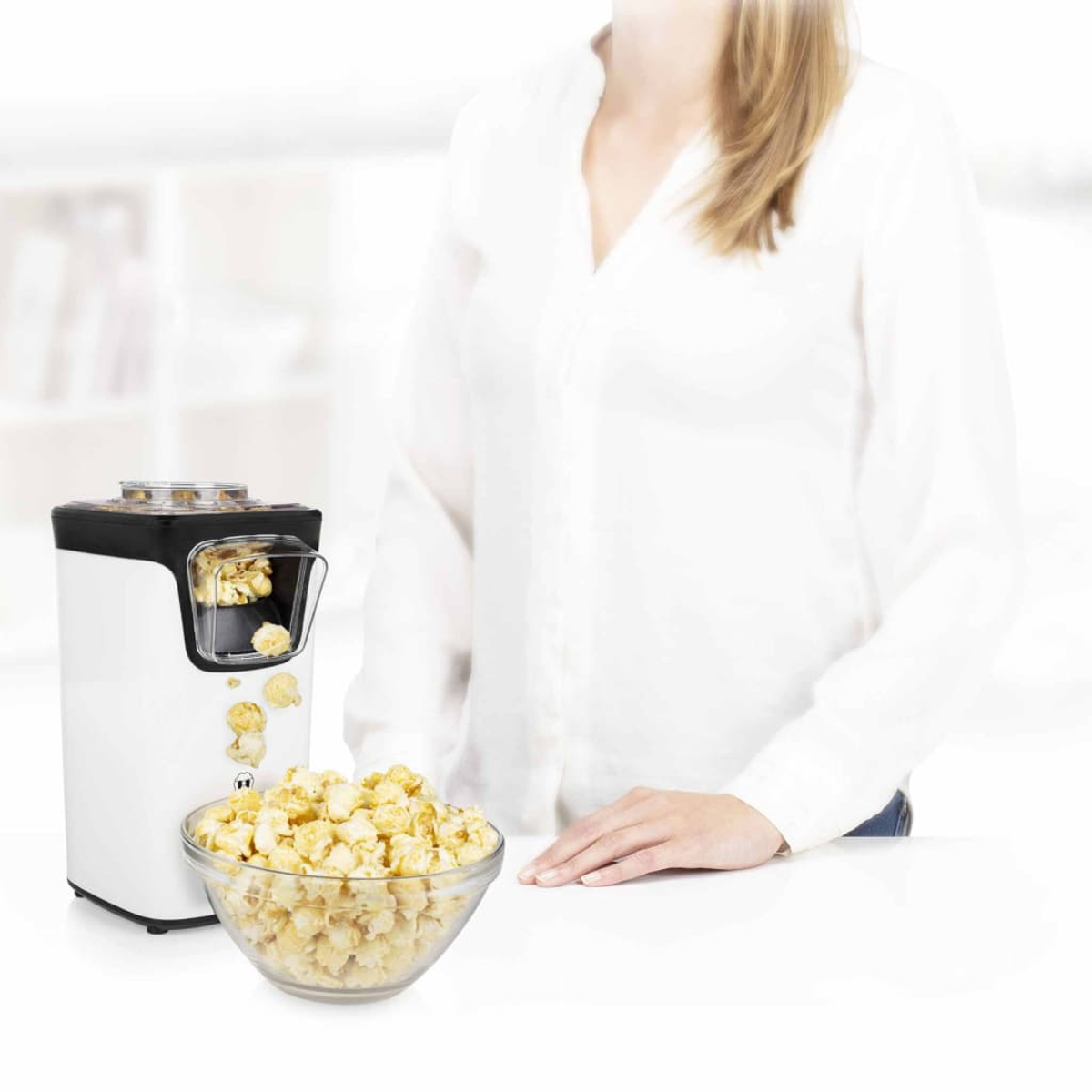 Una macchina per popcorn bianca è su un tavolo, con i popcorn che cadono in una ciotola di vetro.