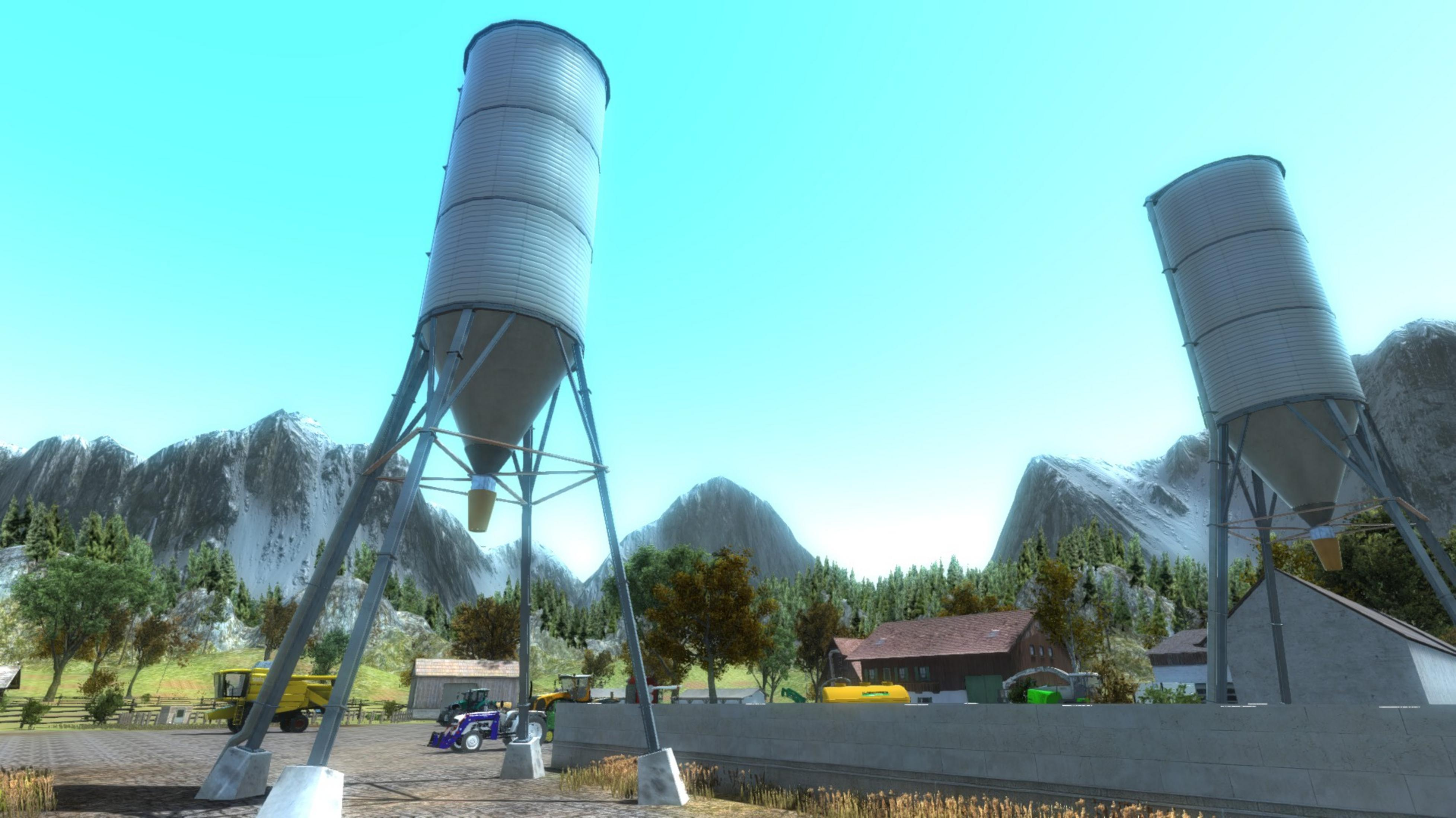 Zwei hohe Silos stehen auf einem Bauernhof mit Bergen im Hintergrund.