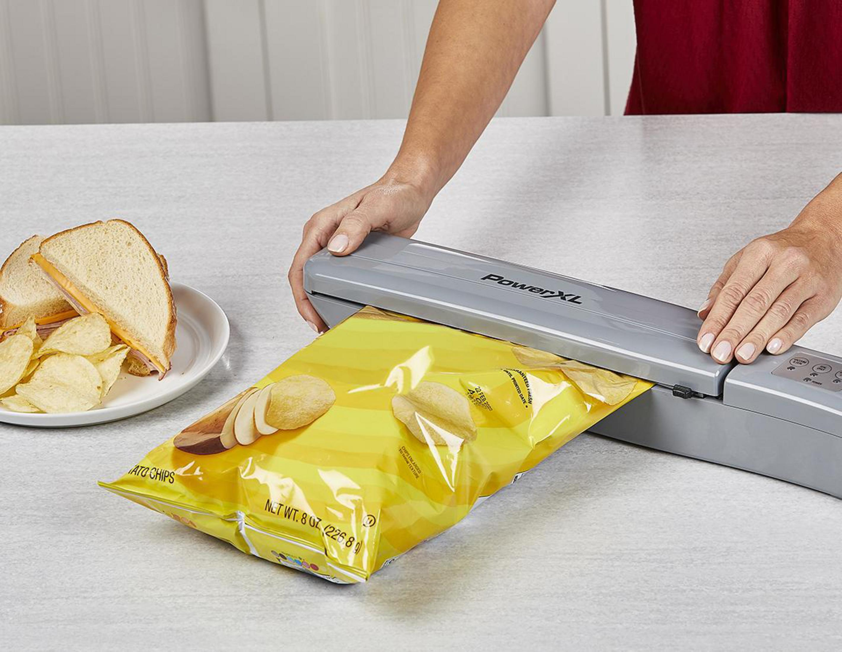 Eine Person benutzt eine Vakuumversiegelungsmaschine für eine Chipstüte neben einem Sandwich.
