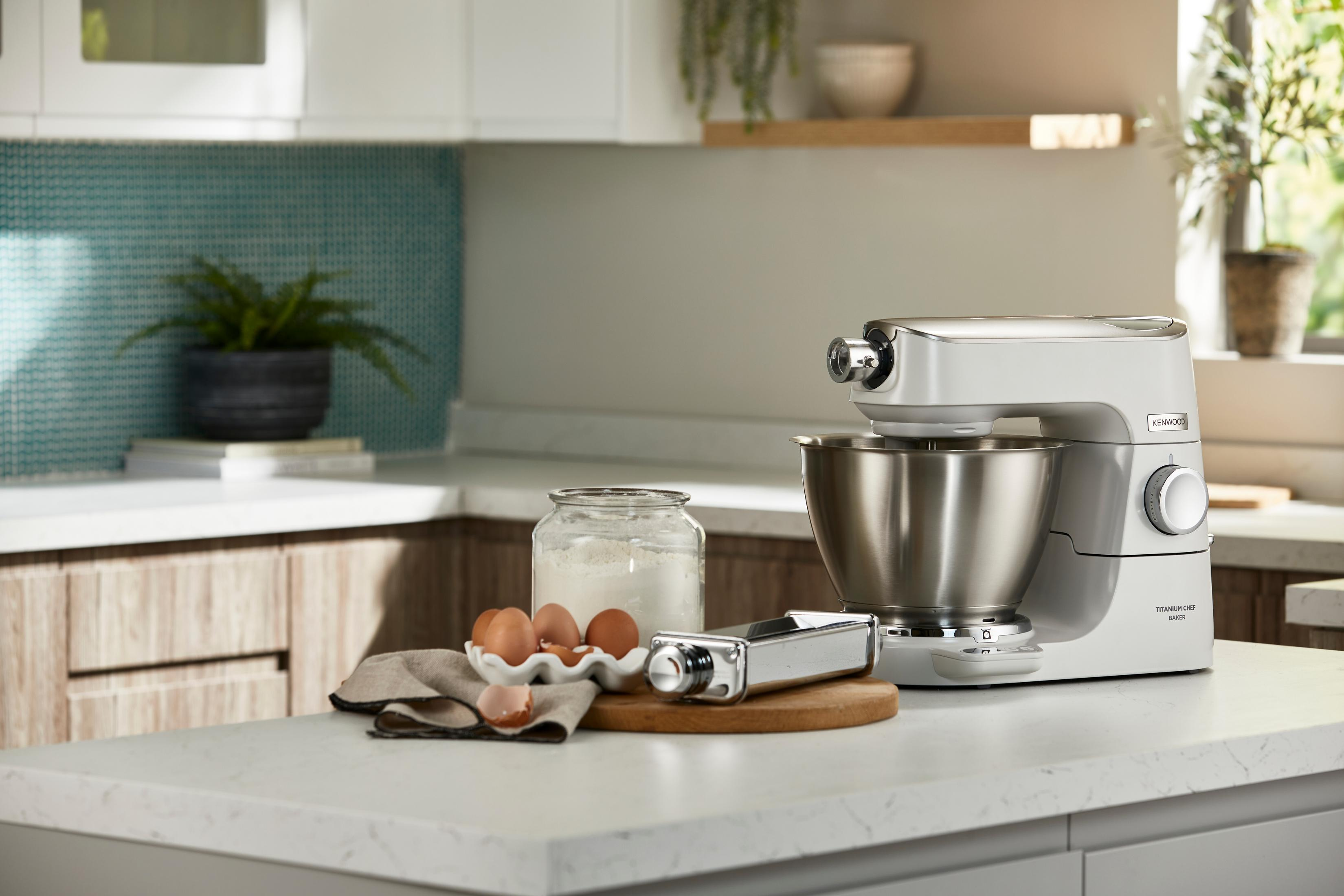 Biały robot Kenwood z misą, jajkami, mąką i przystawką do makaronu.