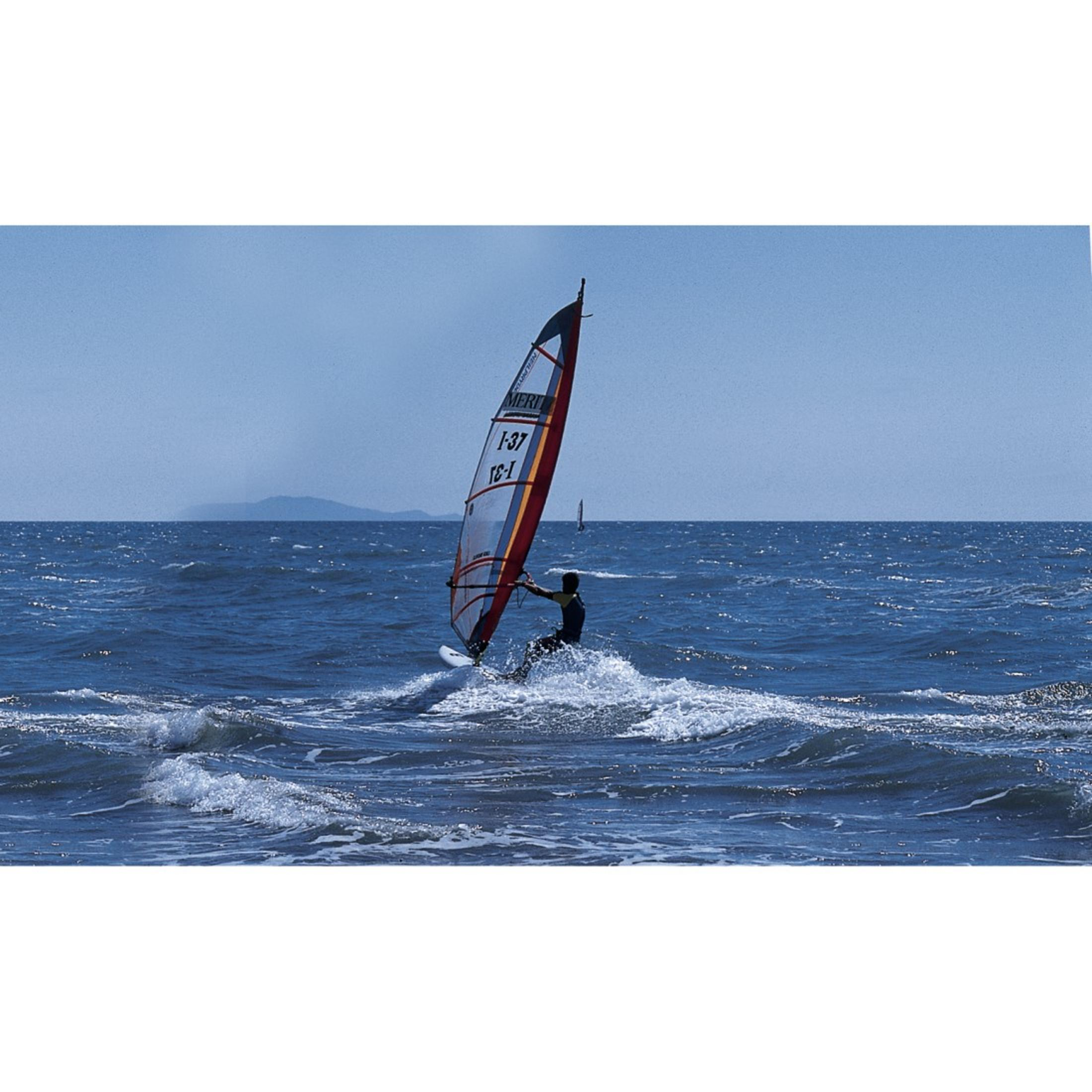Ein Mann auf einem Windsurfbrett surft auf dem blauen Meer mit einer weißen Fahne.