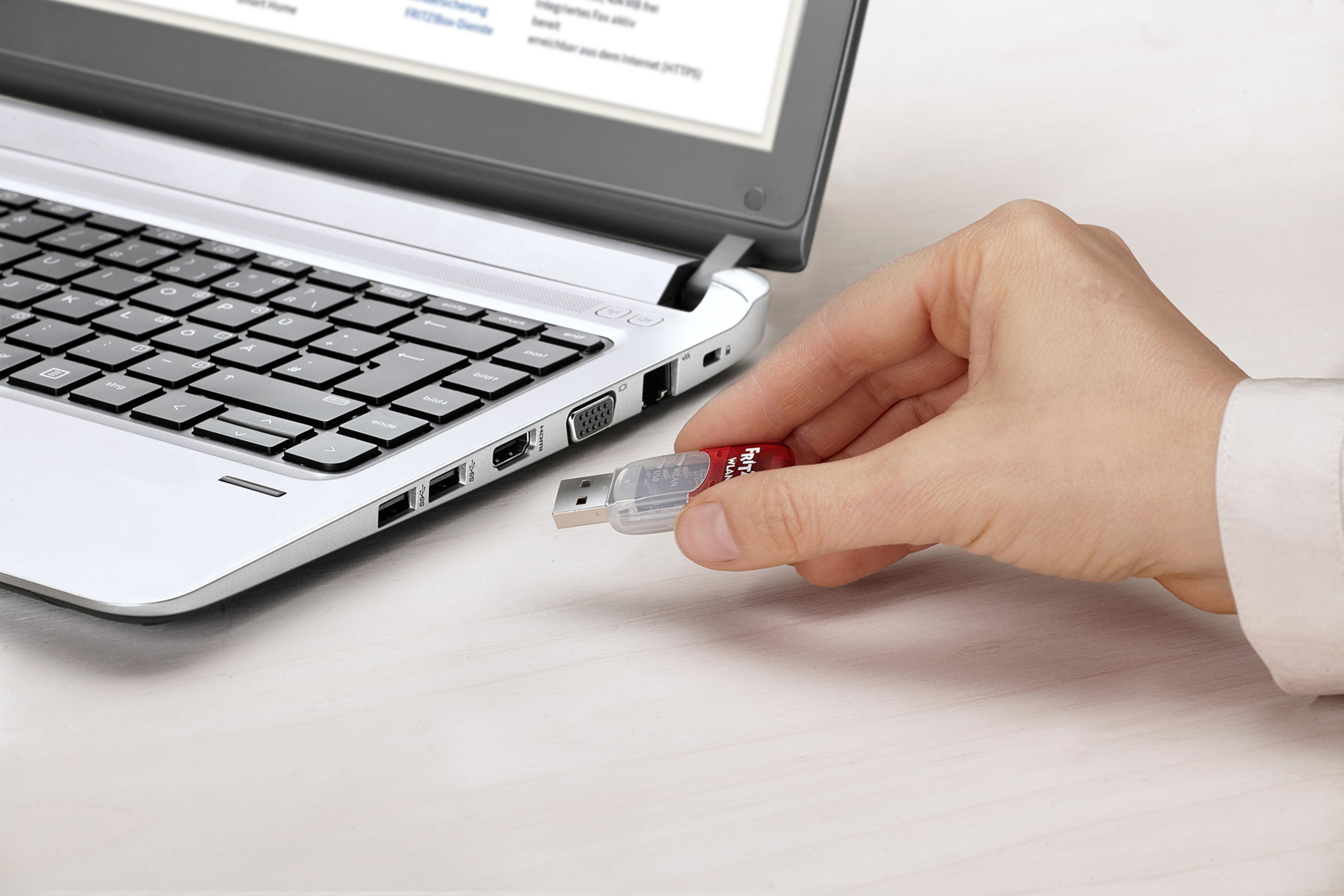 Mano inserisce chiavetta USB in laptop. Persona indossa camicia bianca.