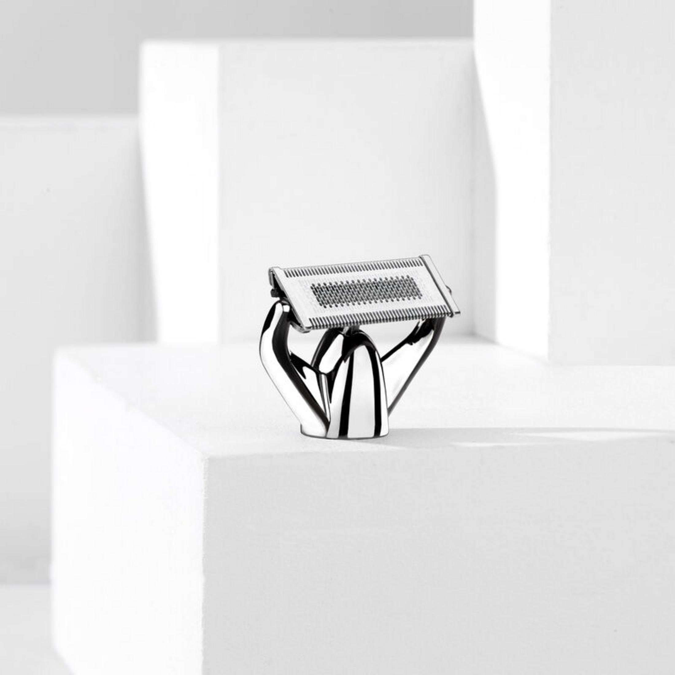 Srebrna maszynka do golenia z metalową siateczką i rączką, na białych blokach.