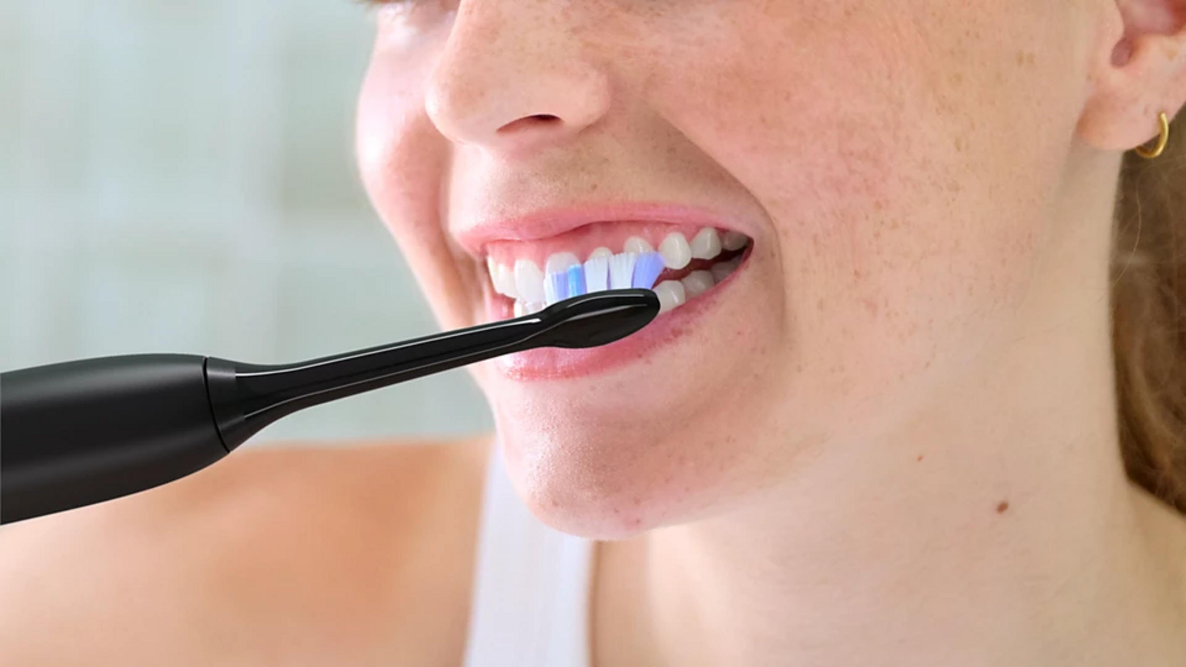 Kobieta myje zęby czarną szczoteczką elektryczną.