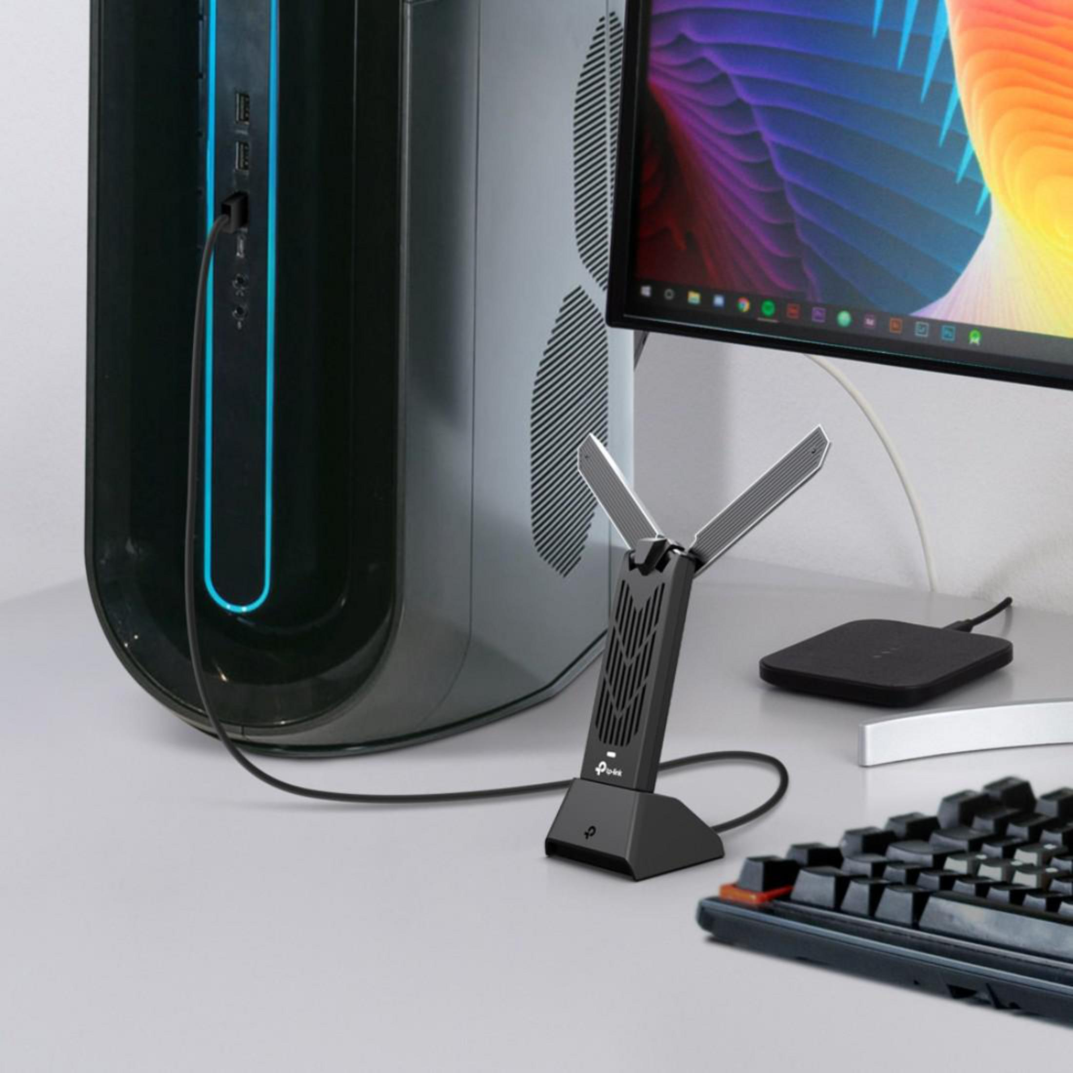 Un adattatore WiFi nero davanti a un PC, con tastiera e pad di ricarica vicini.