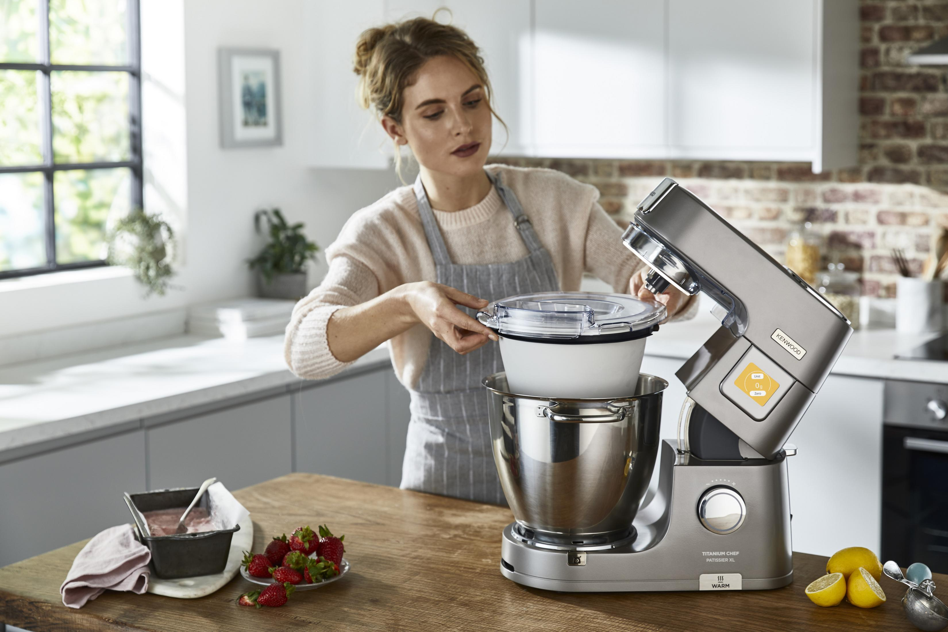 Eine Frau in einer grauen Schürze benutzt eine Küchenmaschine mit Edelstahlschüssel.