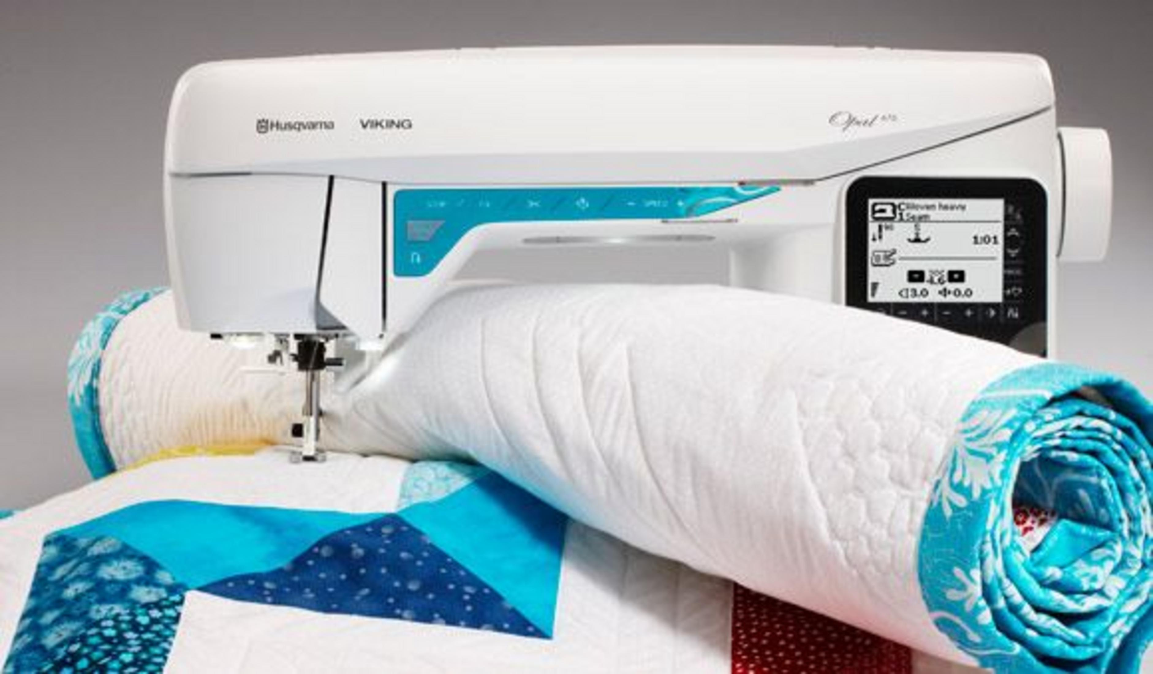 Eine weiße Nähmaschine näht eine bunte Decke mit blauen und weißen Mustern.