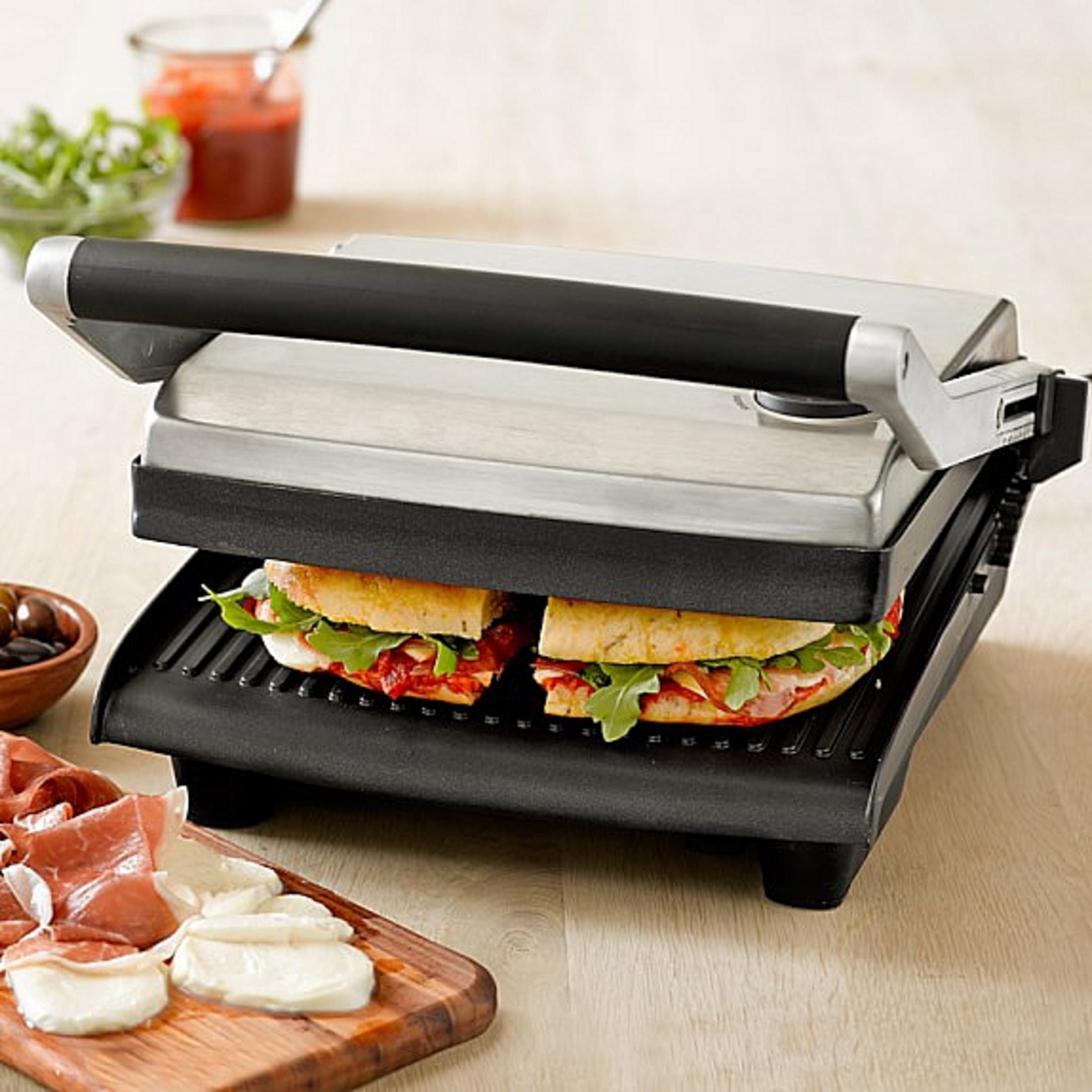 Ein Panini-Grill mit zwei Sandwiches, daneben Schinken und Mozzarella.