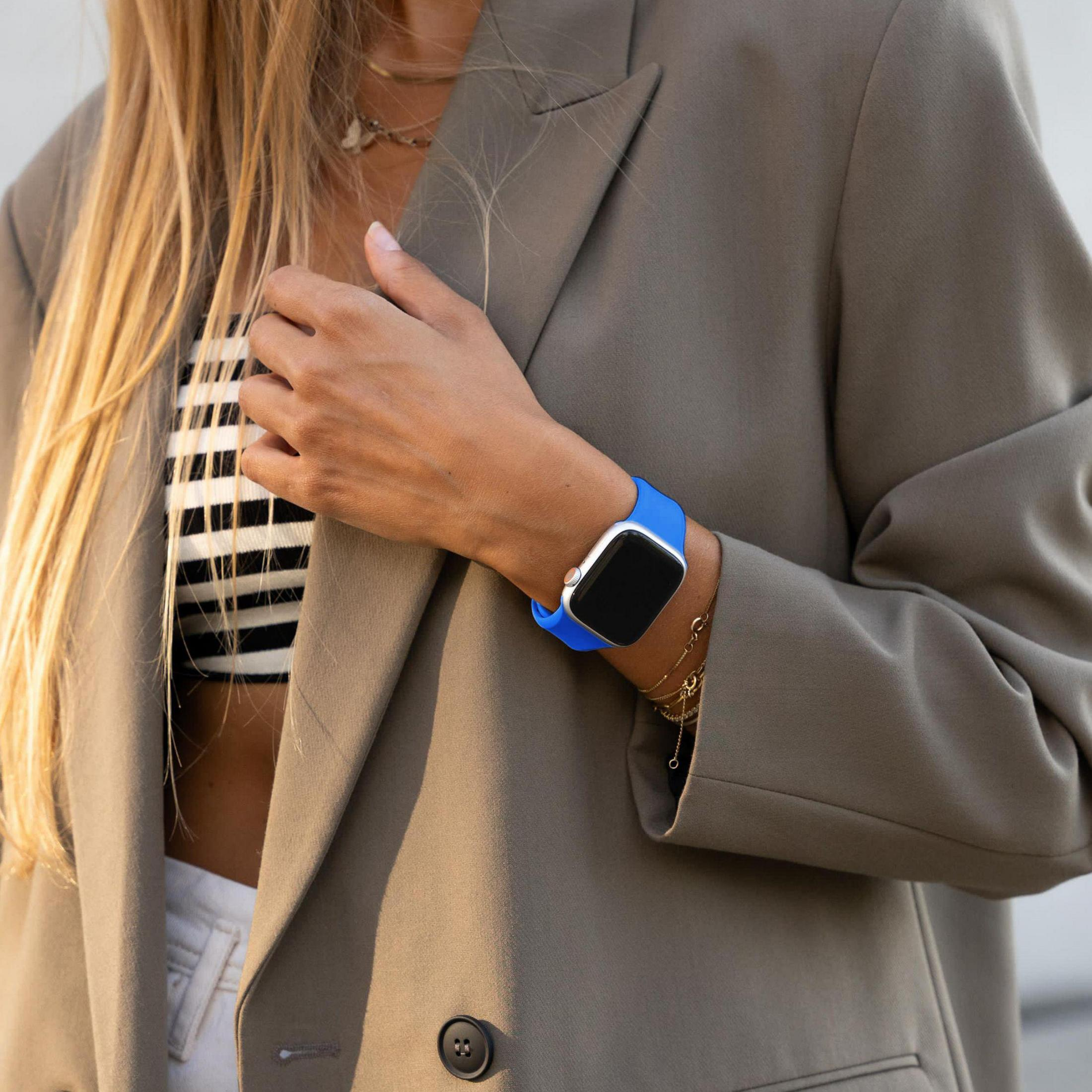 Kobieta nosi brązową kurtkę, pasiasty top i niebieski smartwatch.