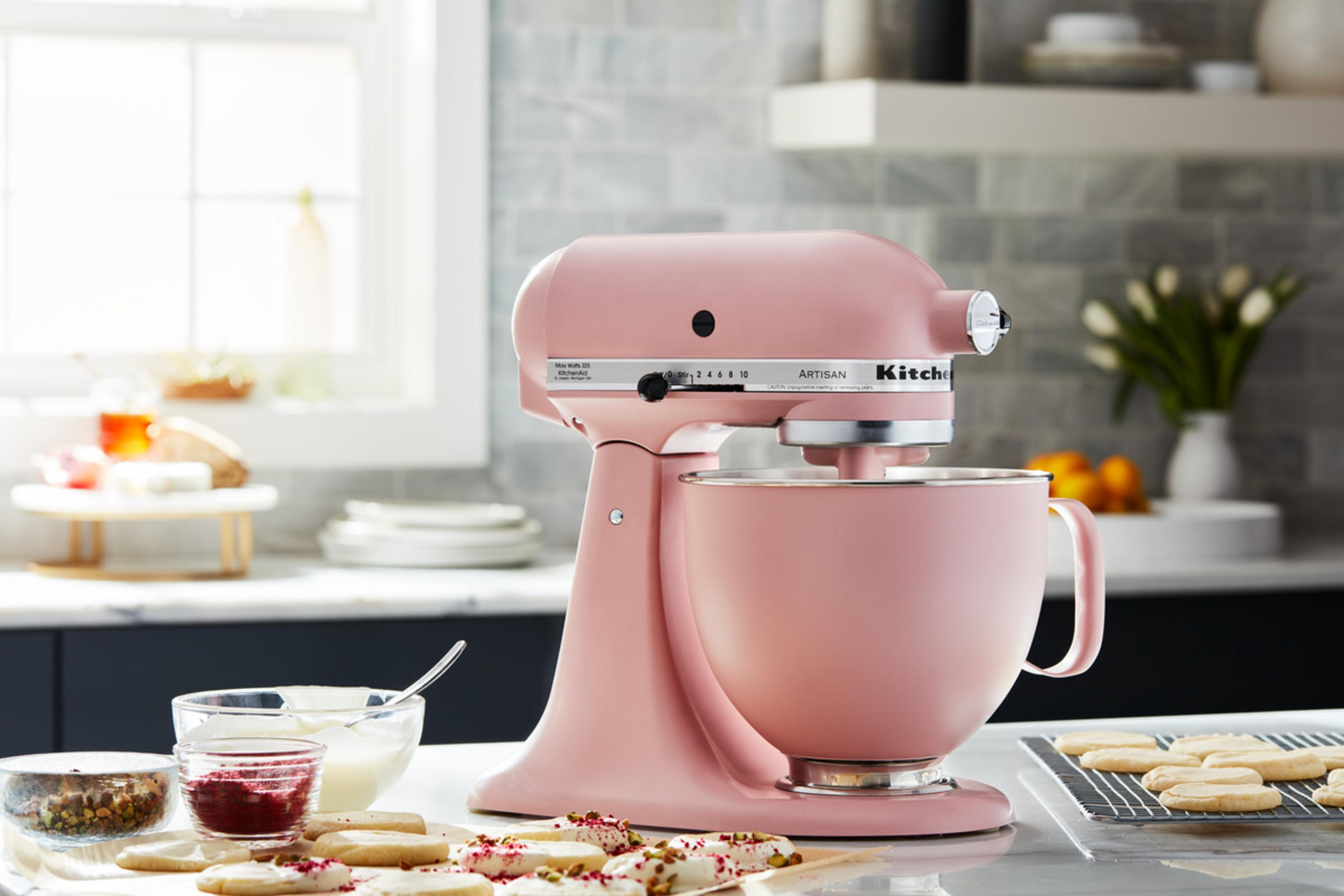 Pembe bir KitchenAid stand mikseri, kase, kurabiye ve malzemeler.