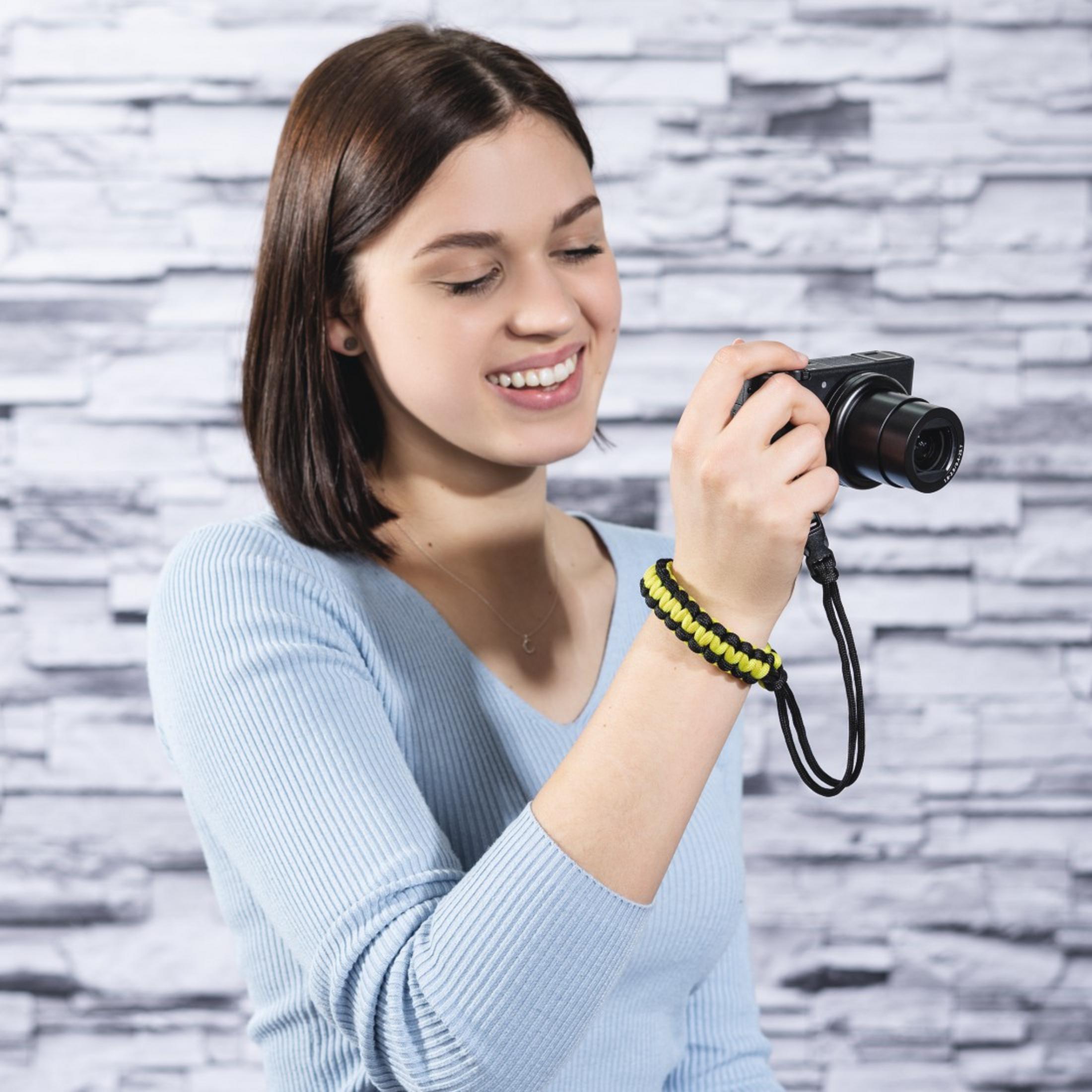 Jeune femme en pull bleu tient un appareil photo et sourit.