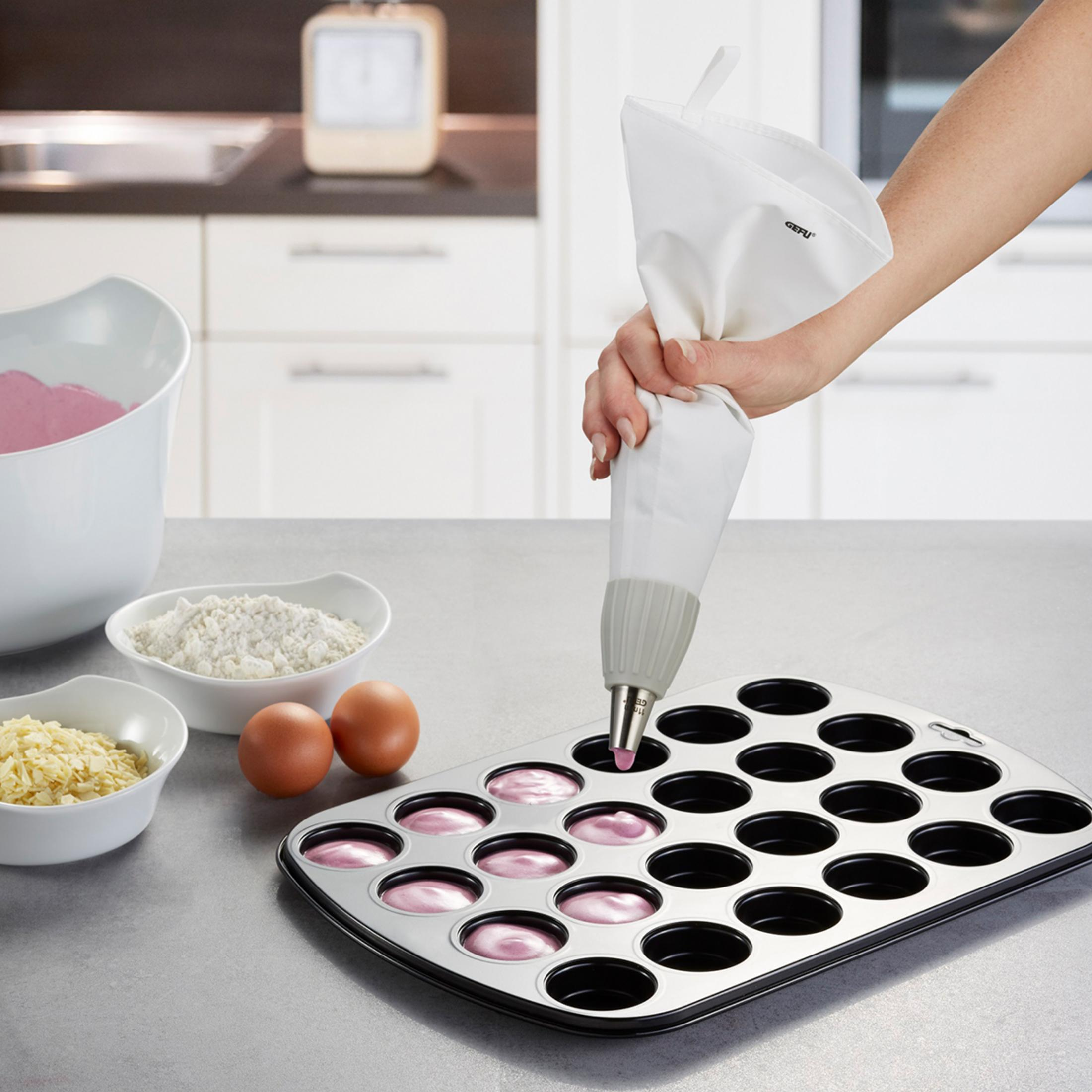Hand füllt Teig mit Spritzbeutel in Muffinform. Zutaten daneben.