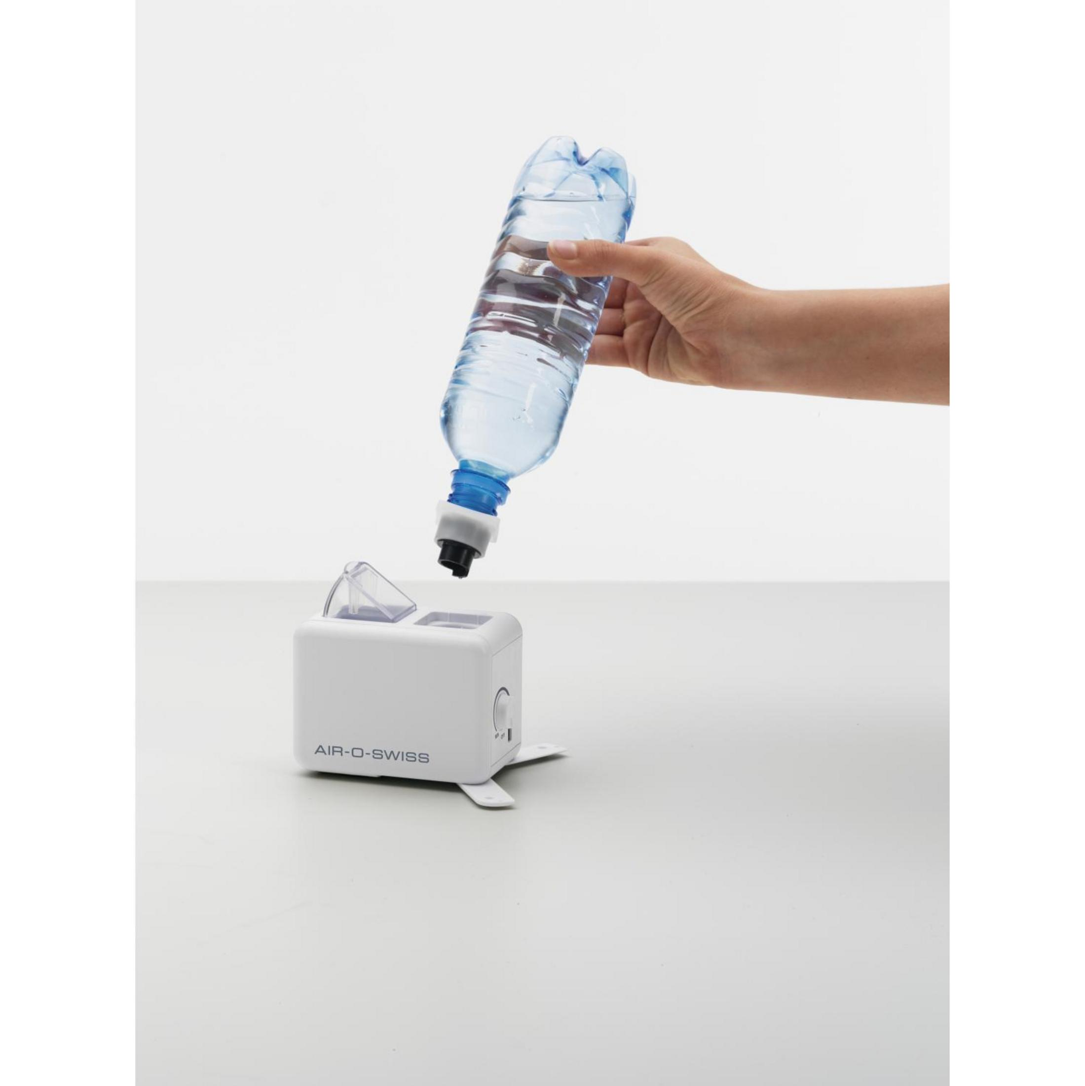 Hand gießt Wasser aus Flasche in weißen Luftbefeuchter.