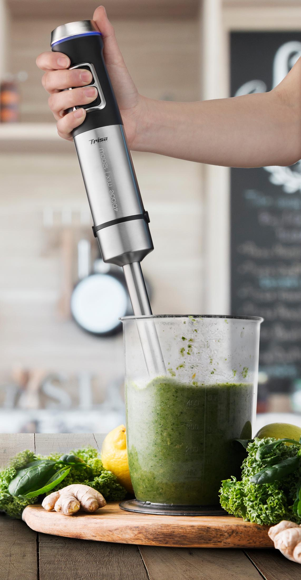 Ein Stabmixer mixt grünen Smoothie in einem Messbecher. Zutaten liegen daneben.