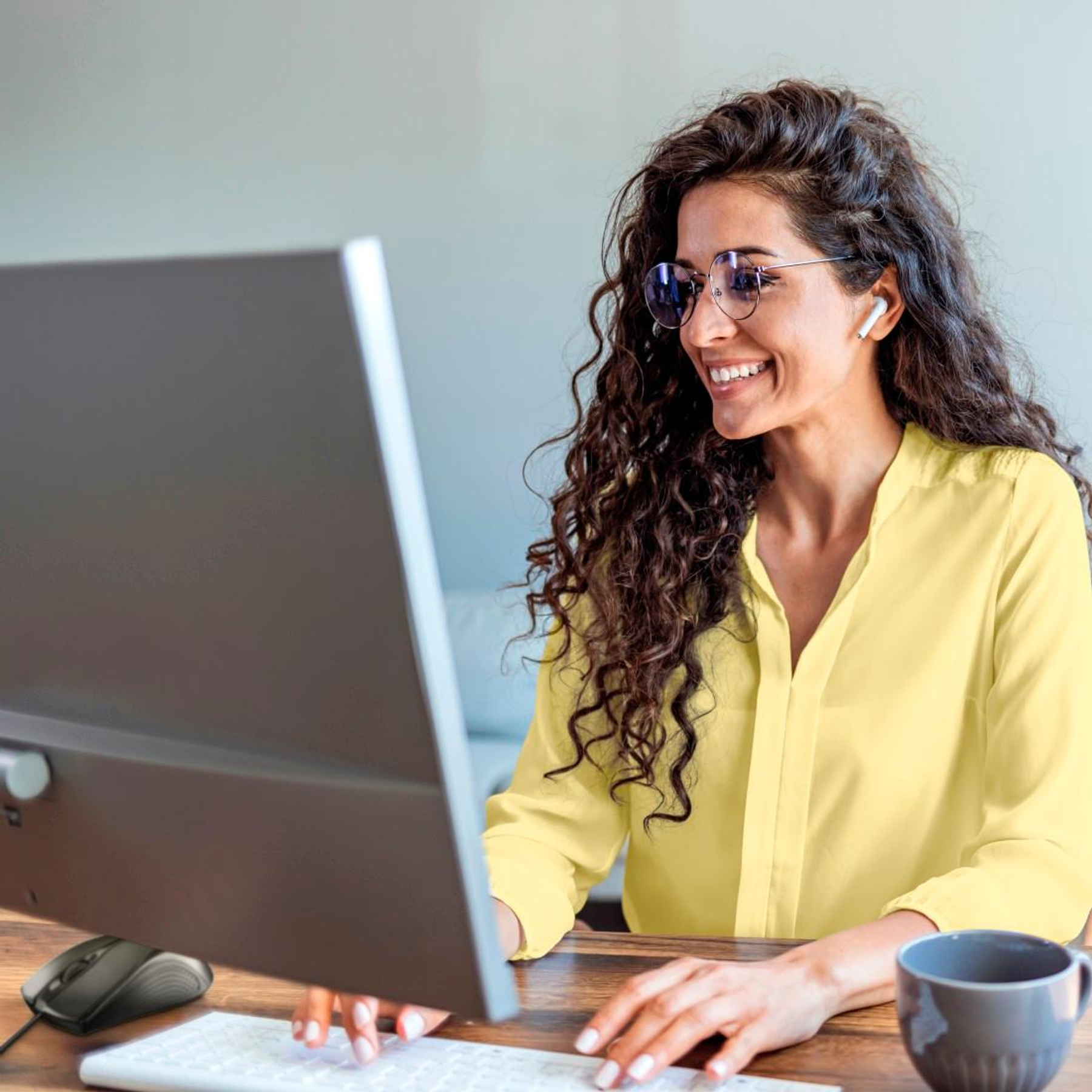 Kobieta z kręconymi włosami w żółtej bluzce siedzi przy biurku.
