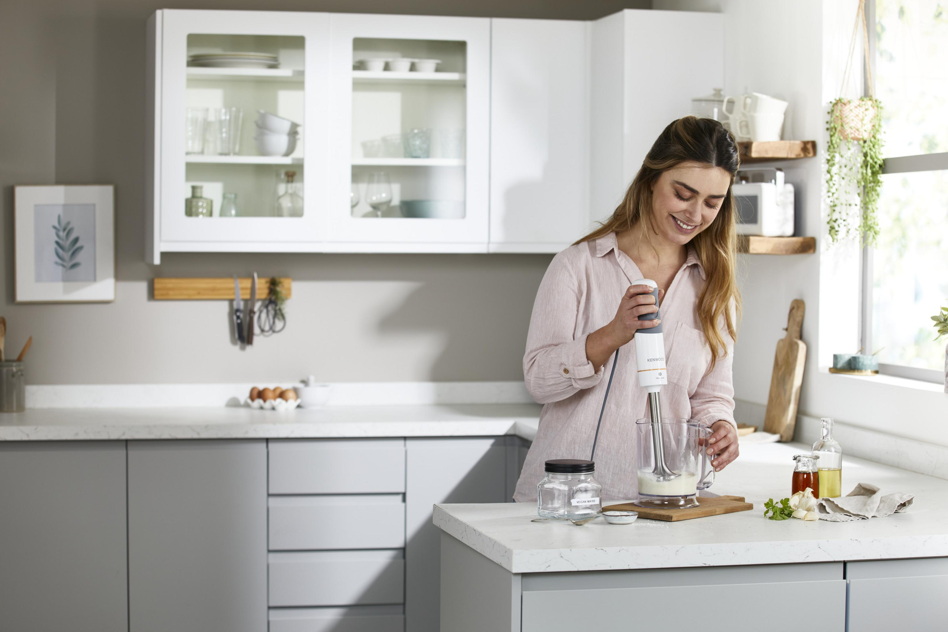 Kobieta miksuje w nowoczesnej kuchni blenderem. Składniki na blacie.