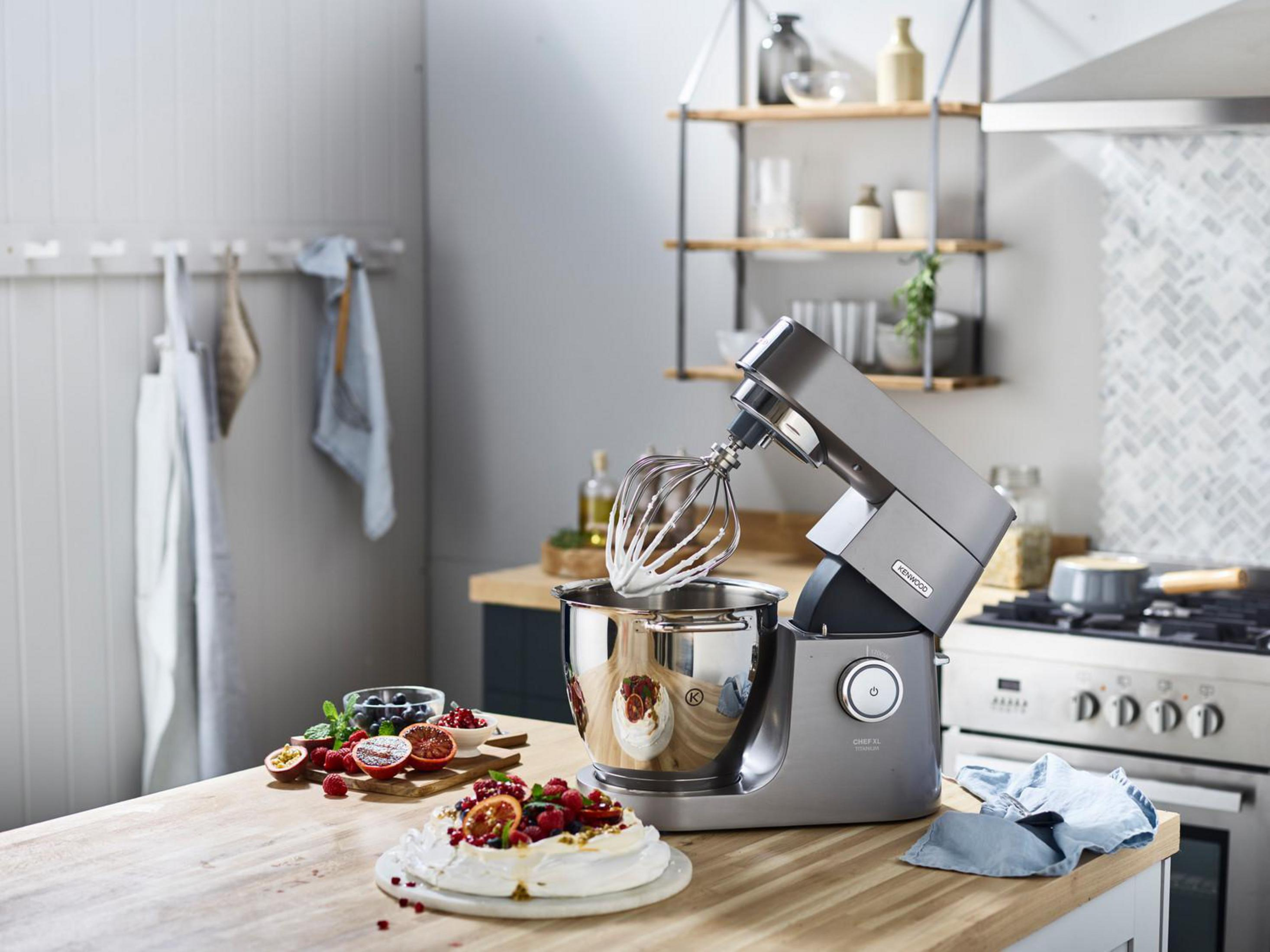 Küchenmaschine mit Schneebesen und Sahne, daneben Pavlova mit Früchten.