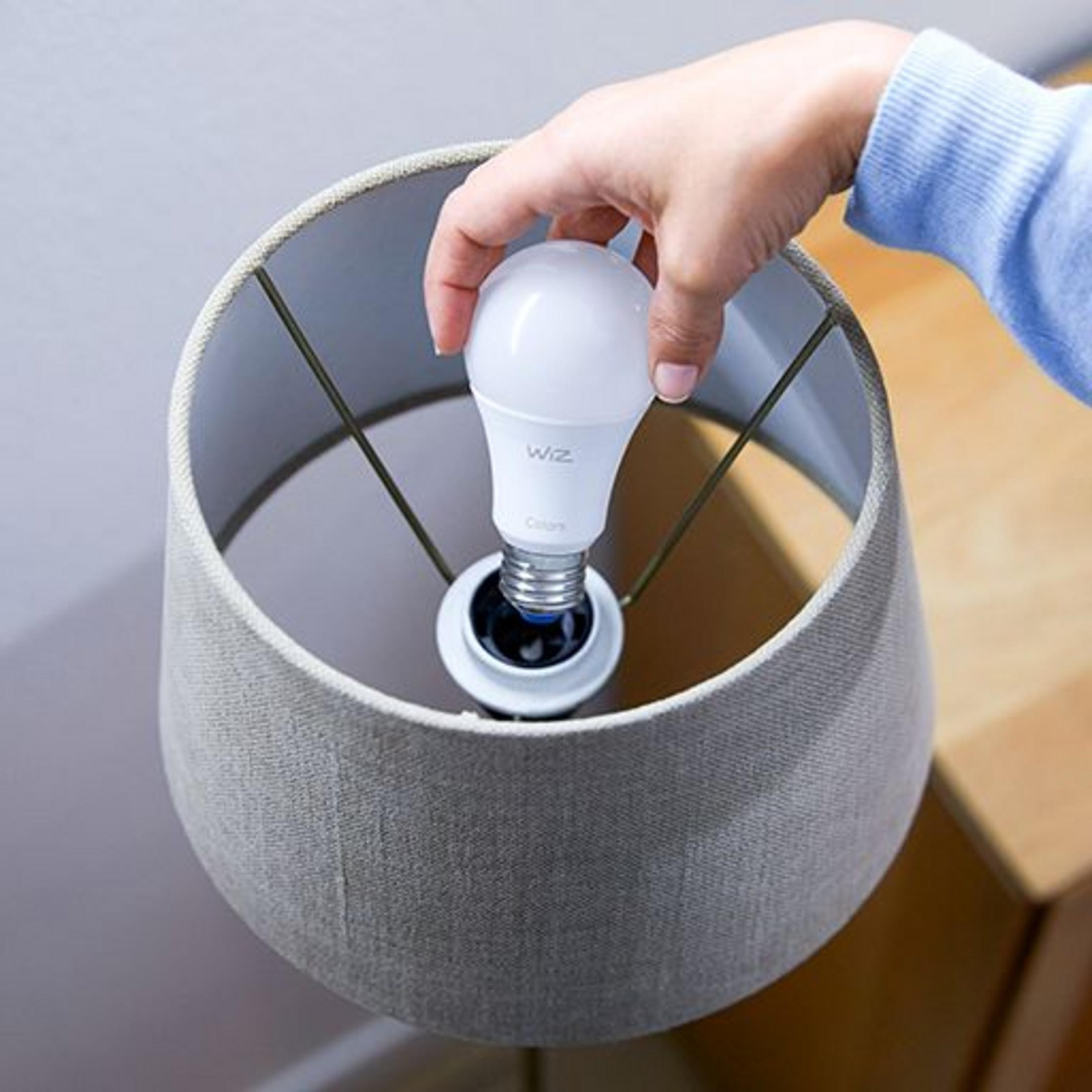 Ręka wkłada białą żarówkę do abażuru.