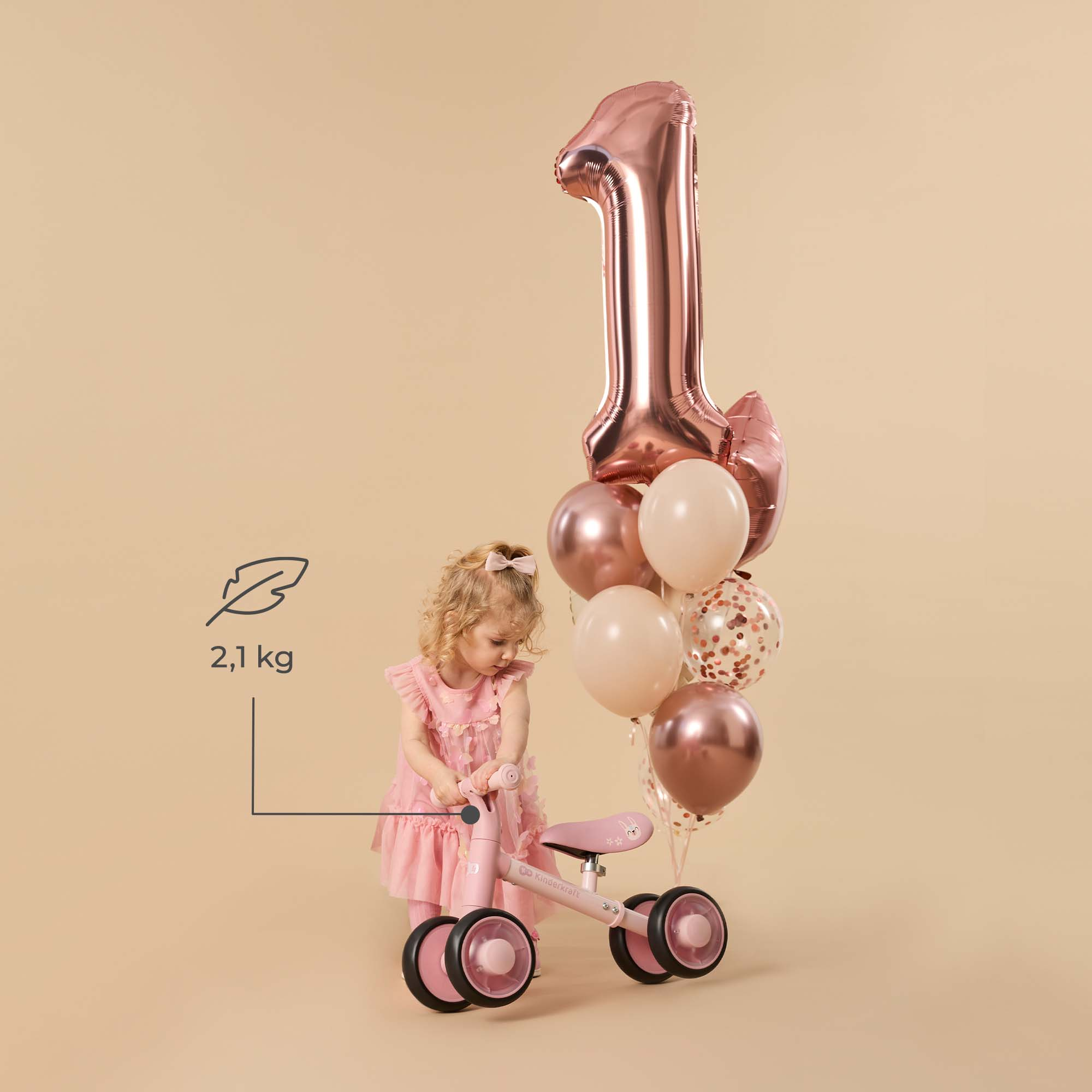 Ein kleines Mädchen in einem rosafarbenen Kleid neben einem Laufrad und Ballons.