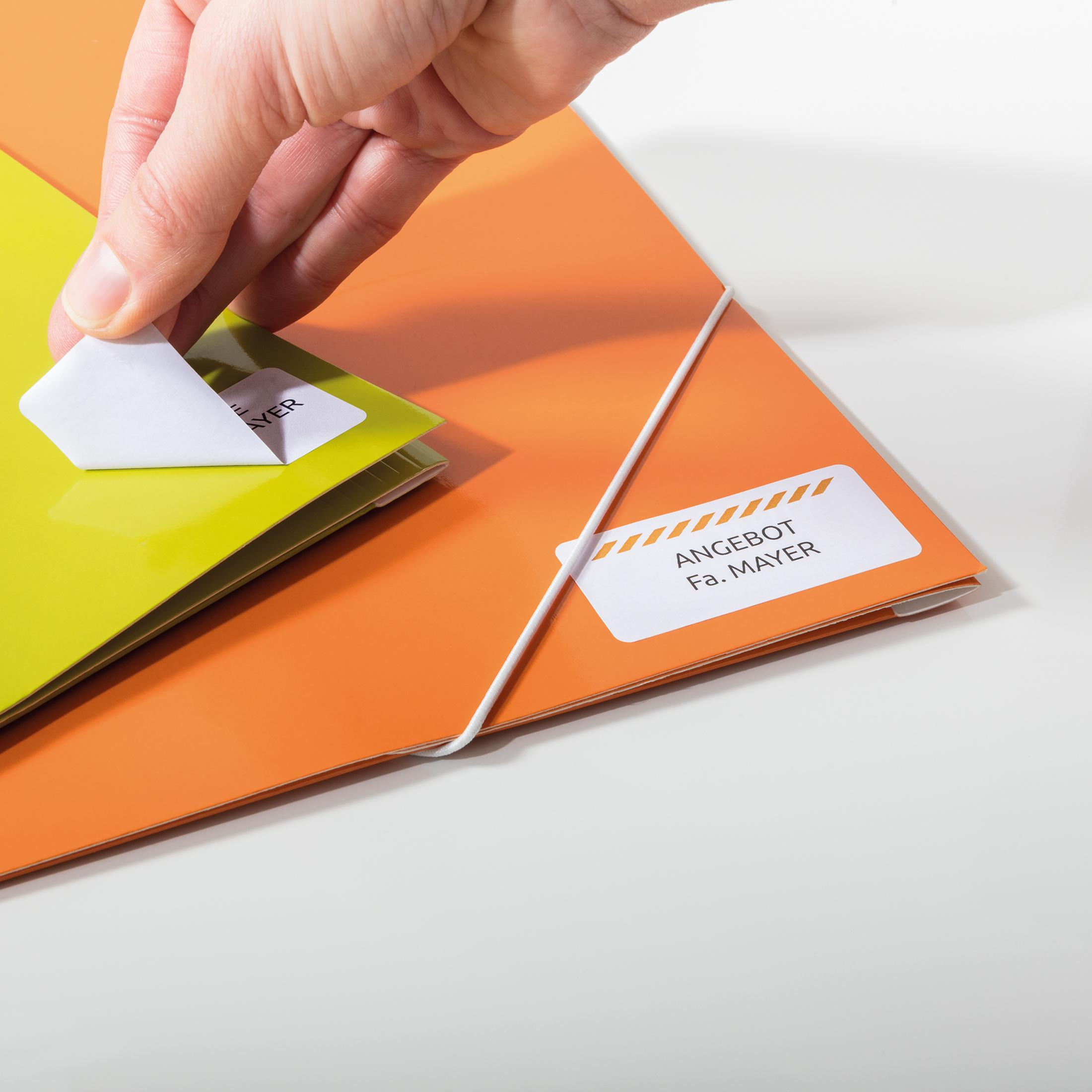 Hand klebt Etikett auf orangefarbene Mappe mit Angebot Fa. Mayer.