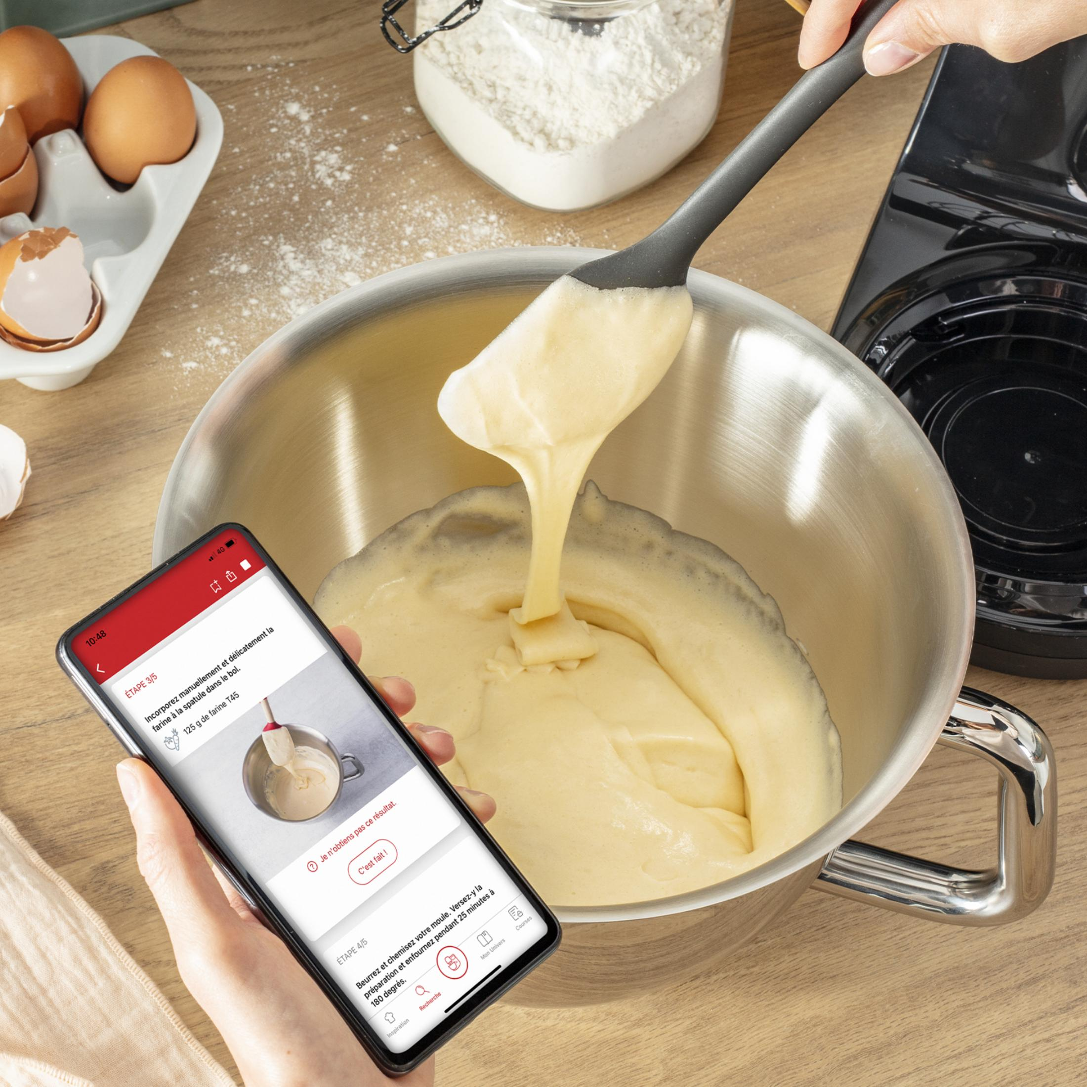 Eine Hand hält ein Handy mit Rezept über einer Rührschüssel mit Teig.