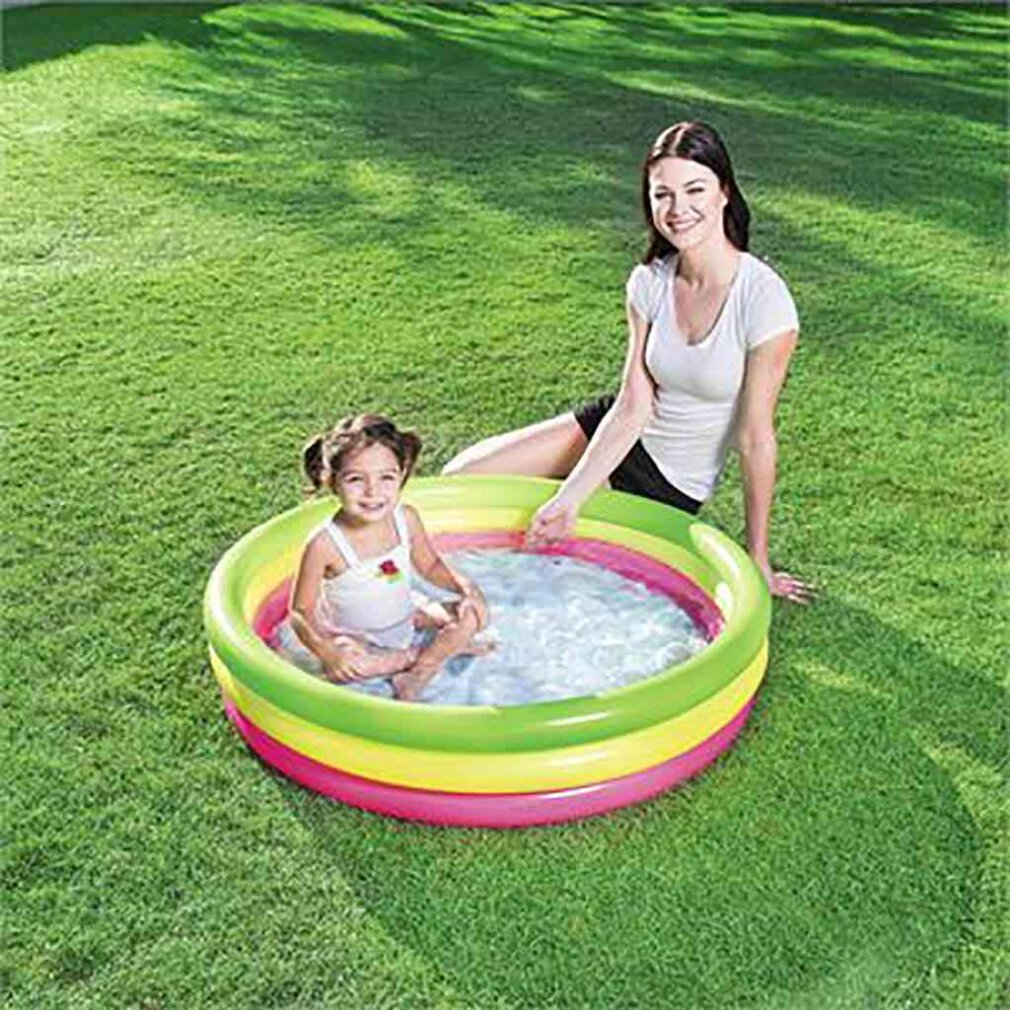 Mujer y niño chapotean en una piscina inflable colorida en el césped.