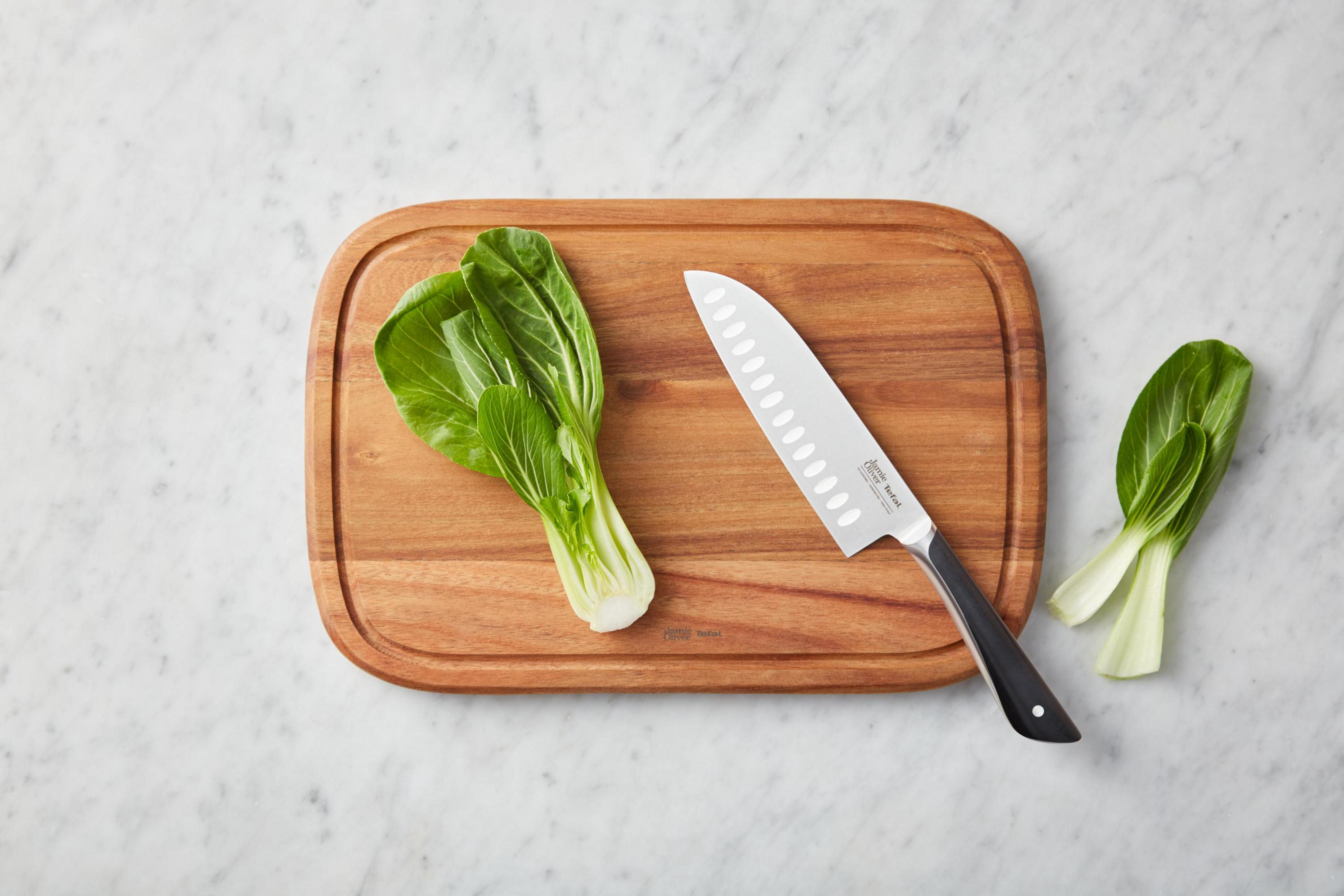 Un coltello da chef e bok choy su un tagliere di legno su marmo.
