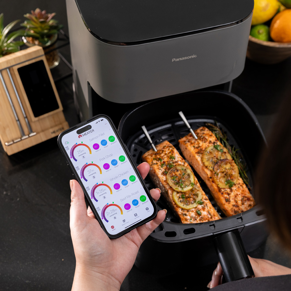Un smartphone affiche des températures de cuisson à côté d'une friteuse à air avec deux filets de saumon.