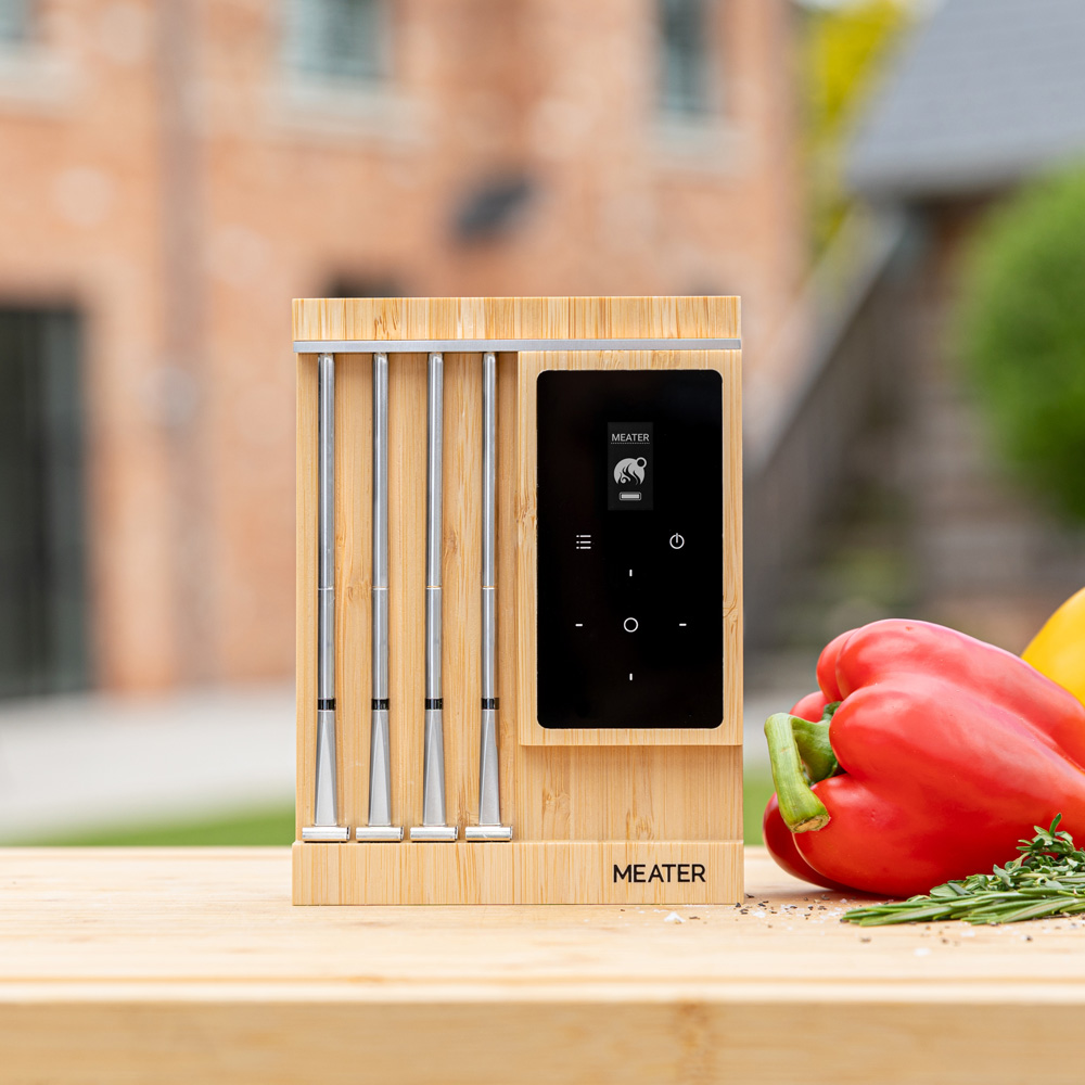 Un support de thermomètre de grill Meater en bois avec quatre sondes à côté d'un poivron rouge.