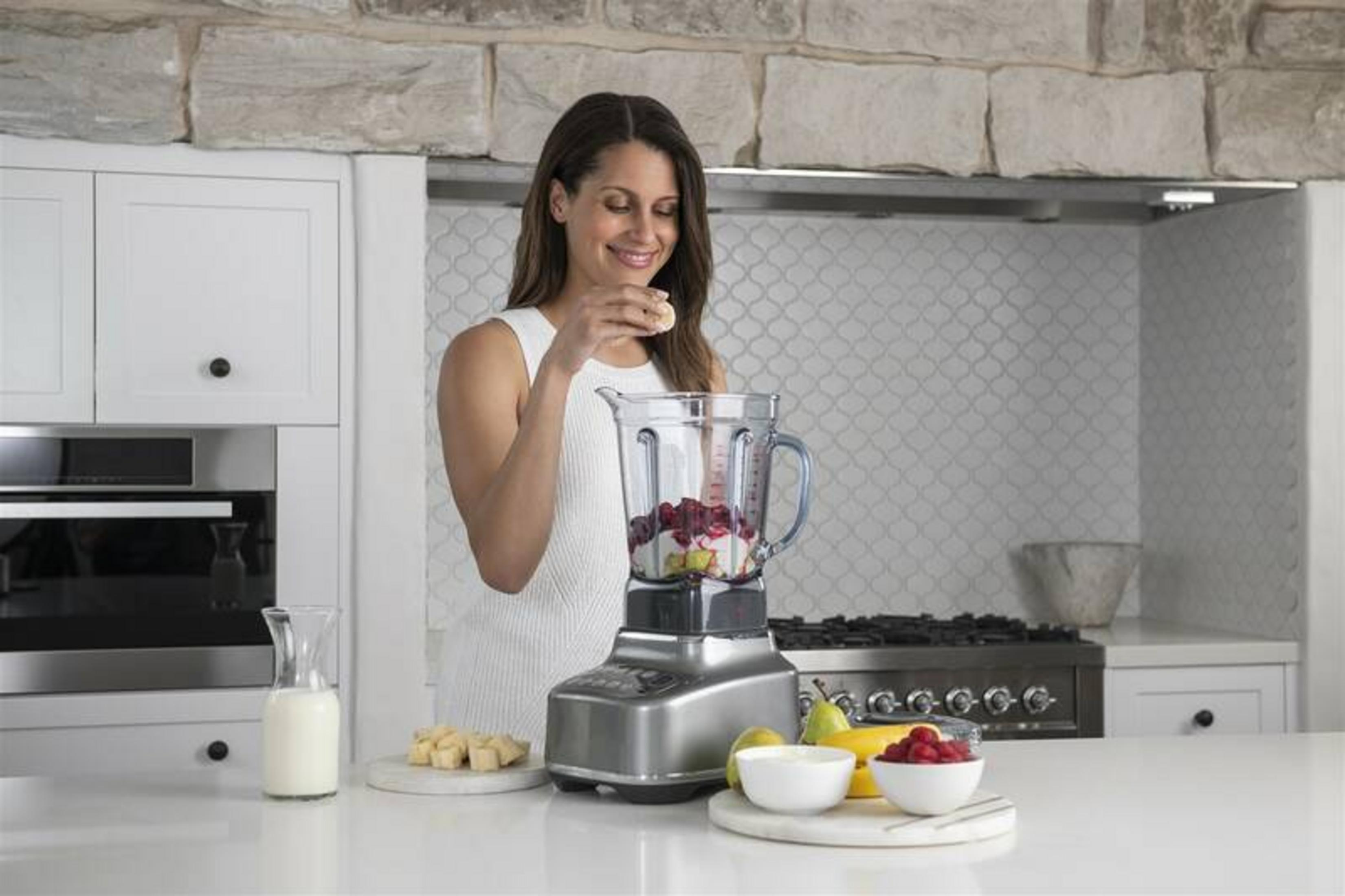 Kobieta dodaje kawałki banana do blendera z owocami i lodem.