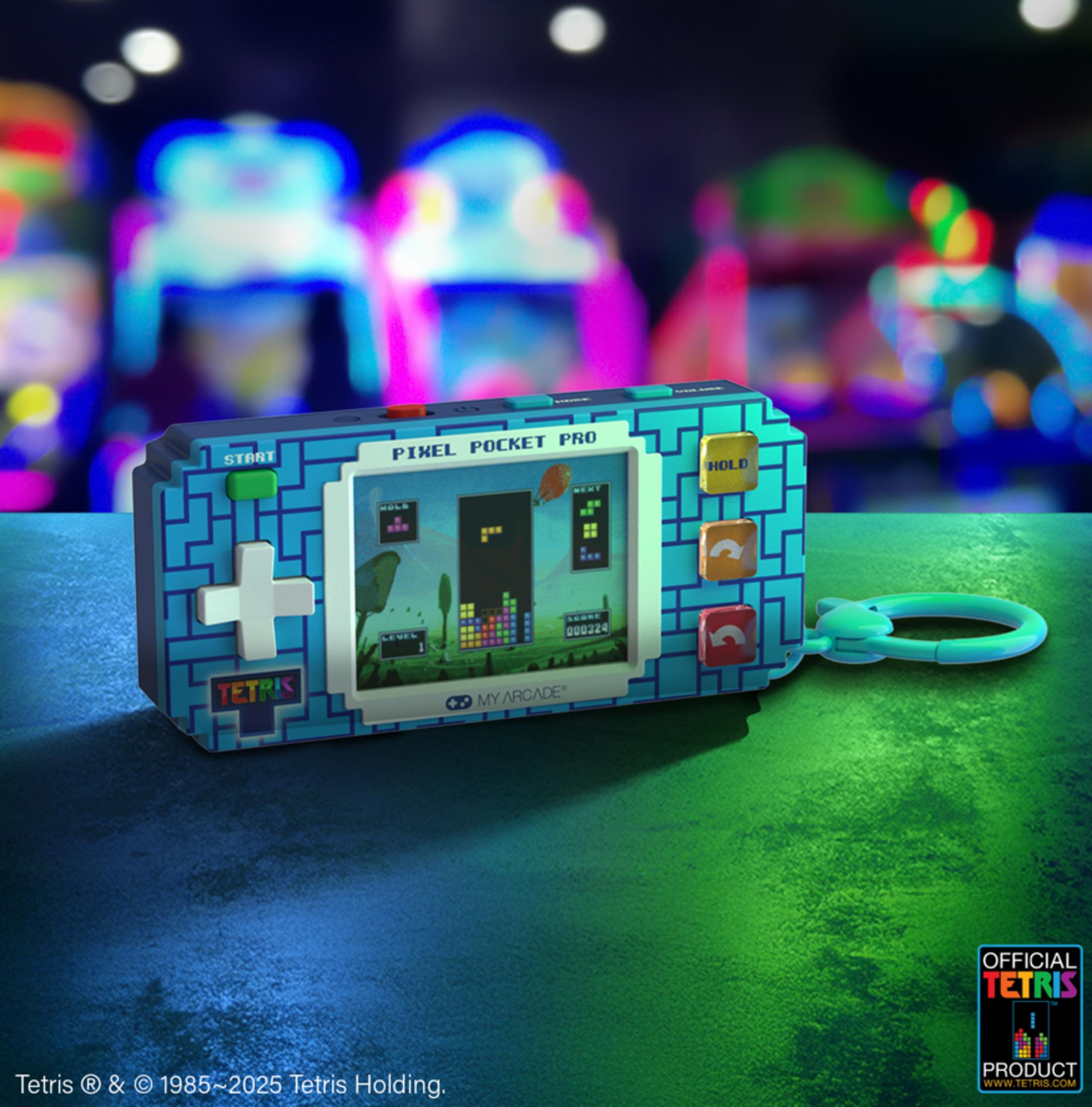 Un dispositivo di gioco portatile Tetris blu con portachiavi poggia su una superficie verde e blu.