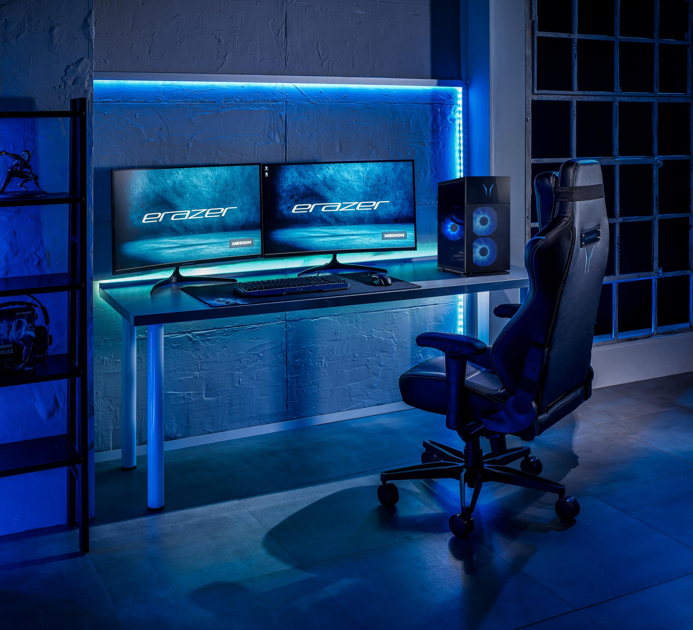 Ein Gaming-Setup mit zwei Monitoren, einem PC und einem Stuhl, beleuchtet von blauen LEDs.