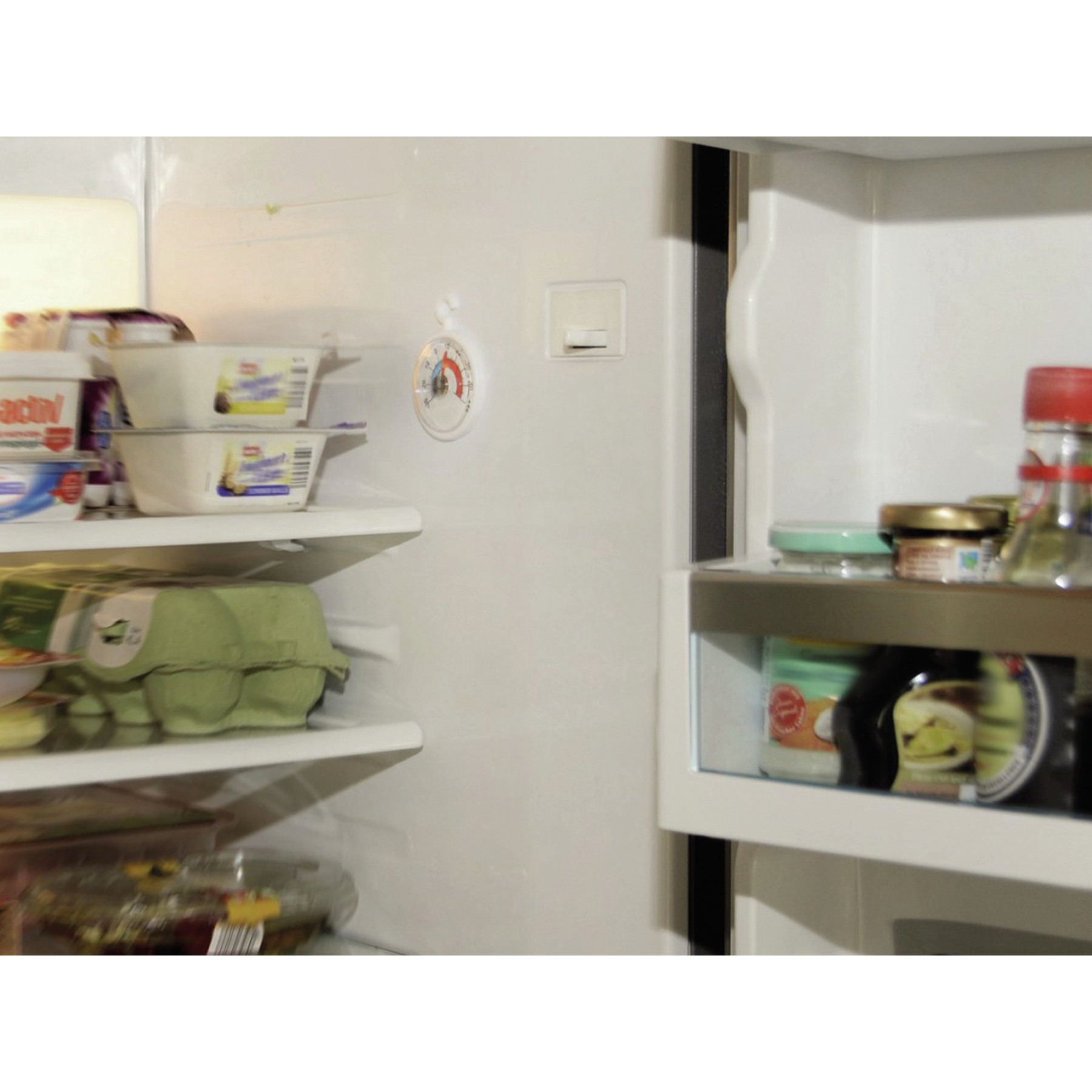 Offener Kühlschrank mit Lebensmitteln auf Regalen, Eierkarton und Thermometer.