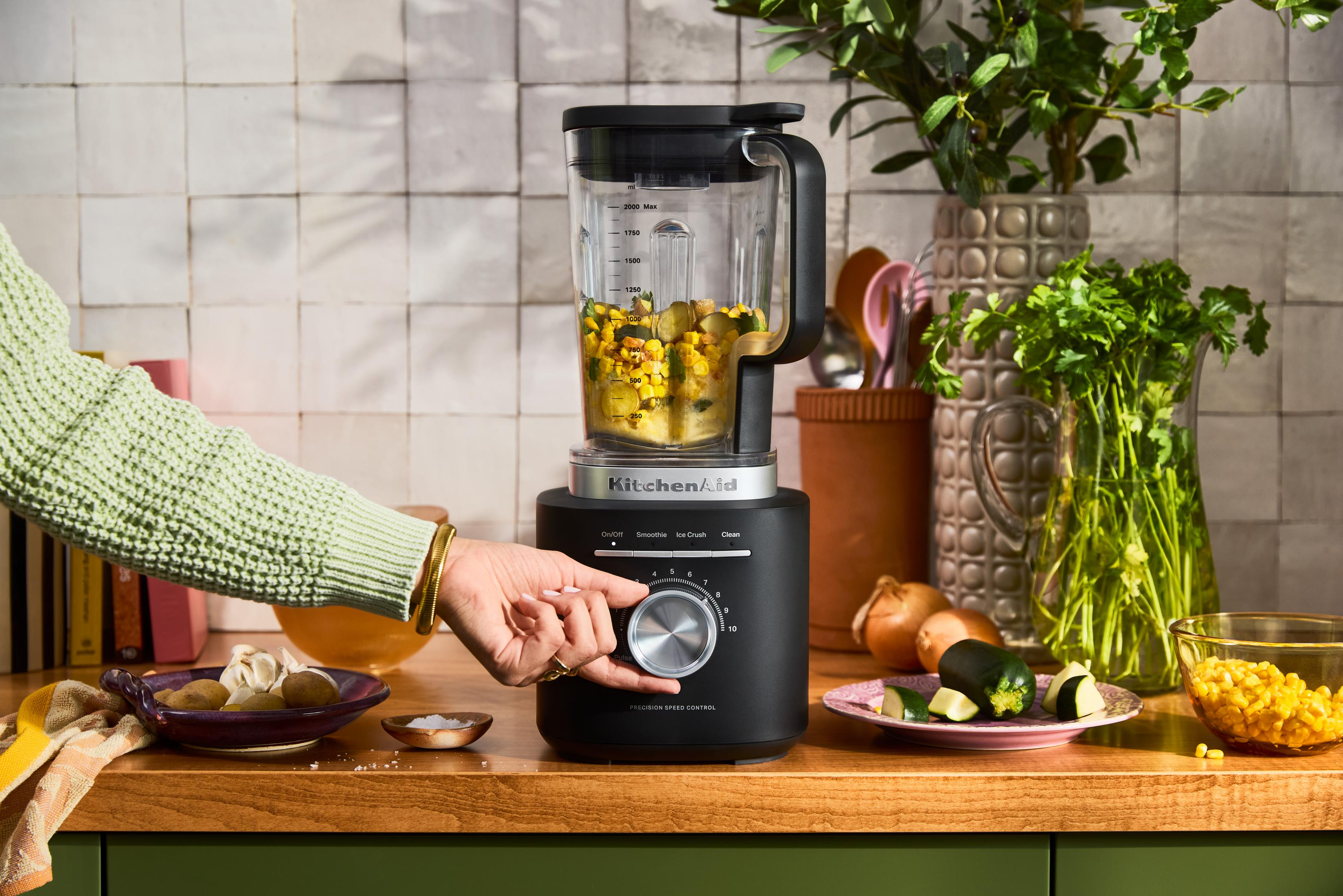 Una mano regola un frullatore KitchenAid nero con ingredienti.