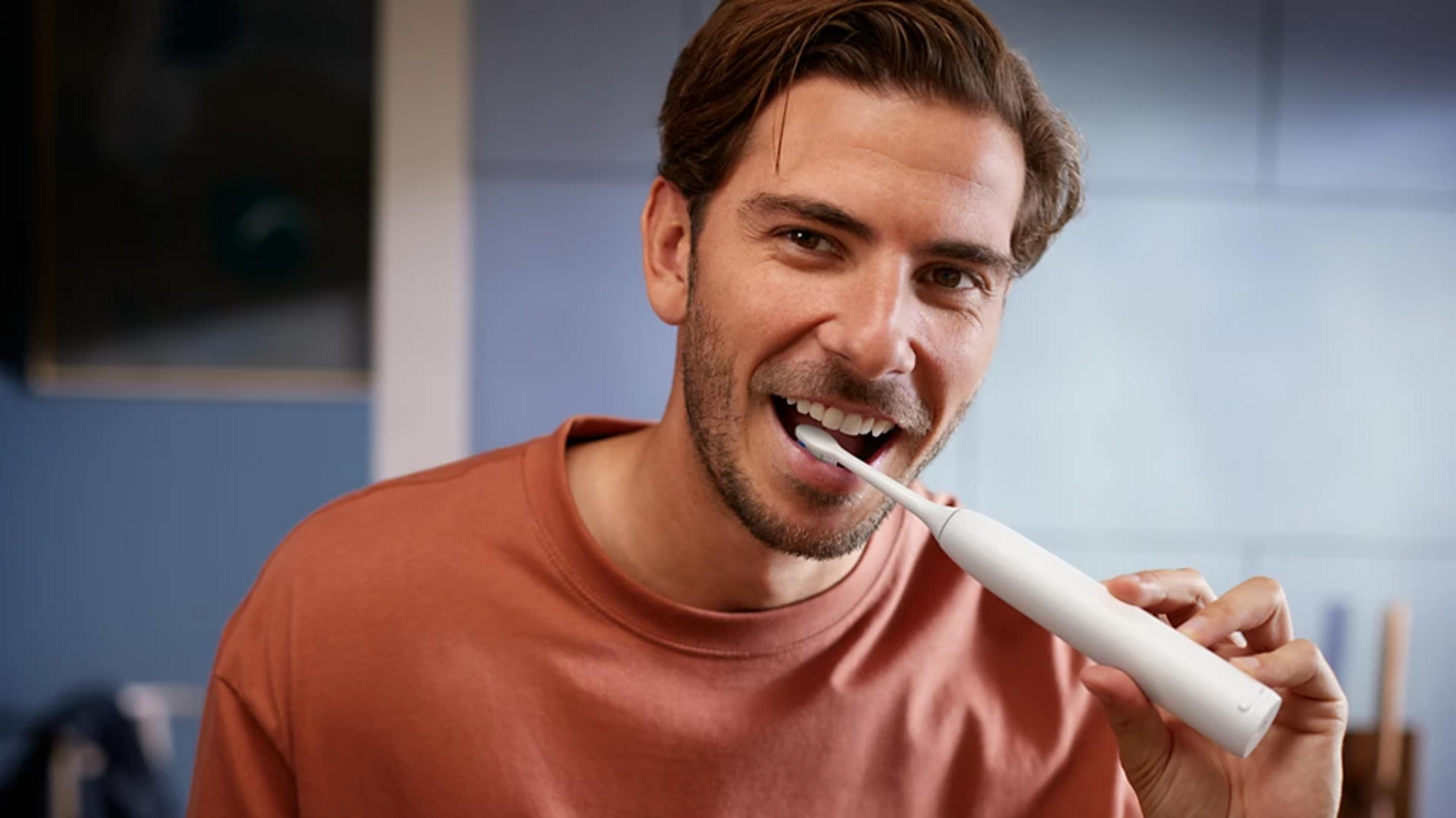 Mężczyzna myje zęby szczoteczką elektryczną.