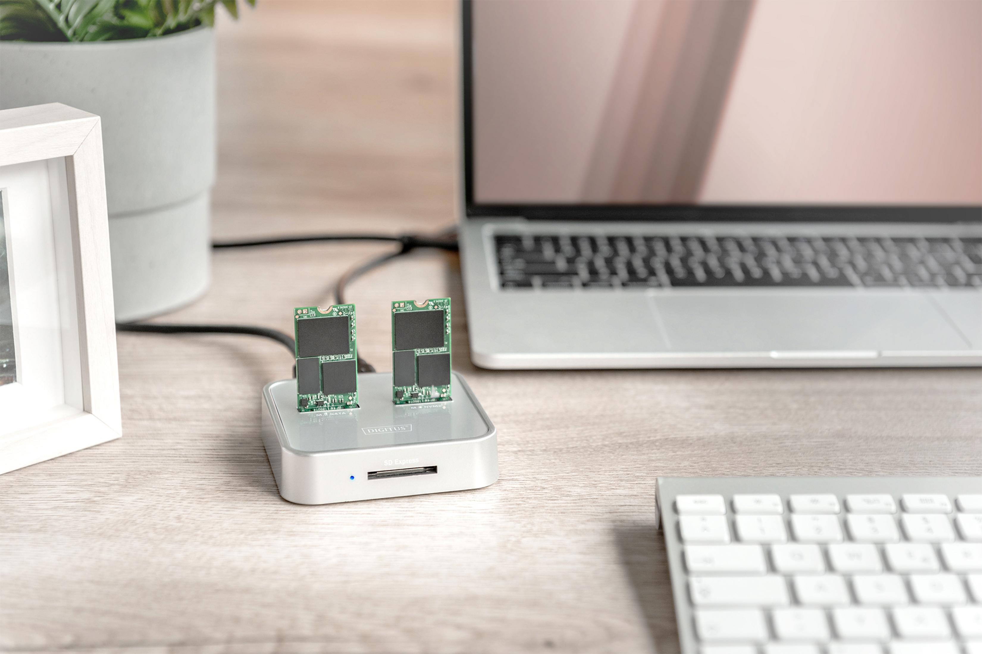 Due SSD in un dock, laptop e tastiera su una scrivania di legno.