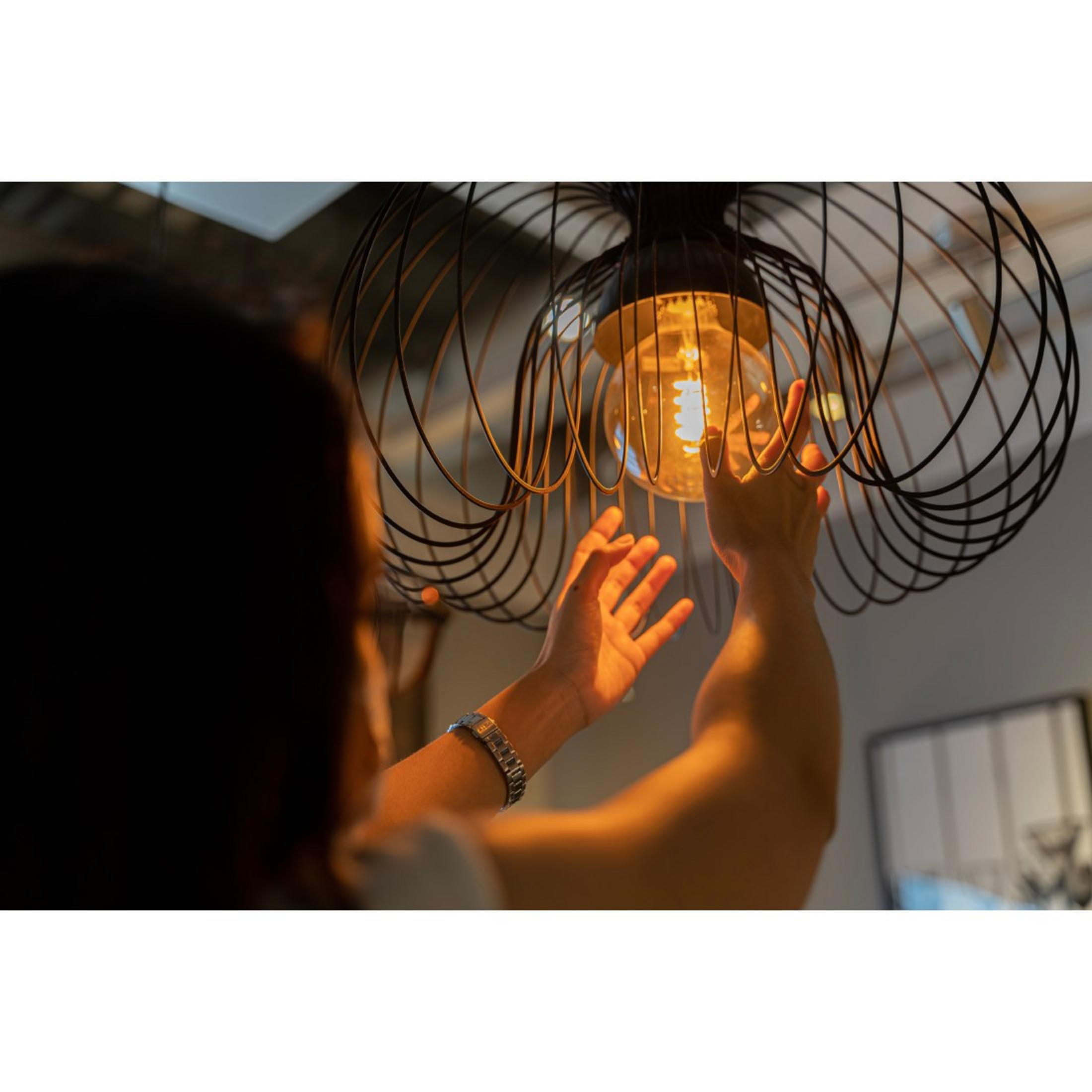 Una persona tocca una lampadina all'interno di un paralume in filo metallico.