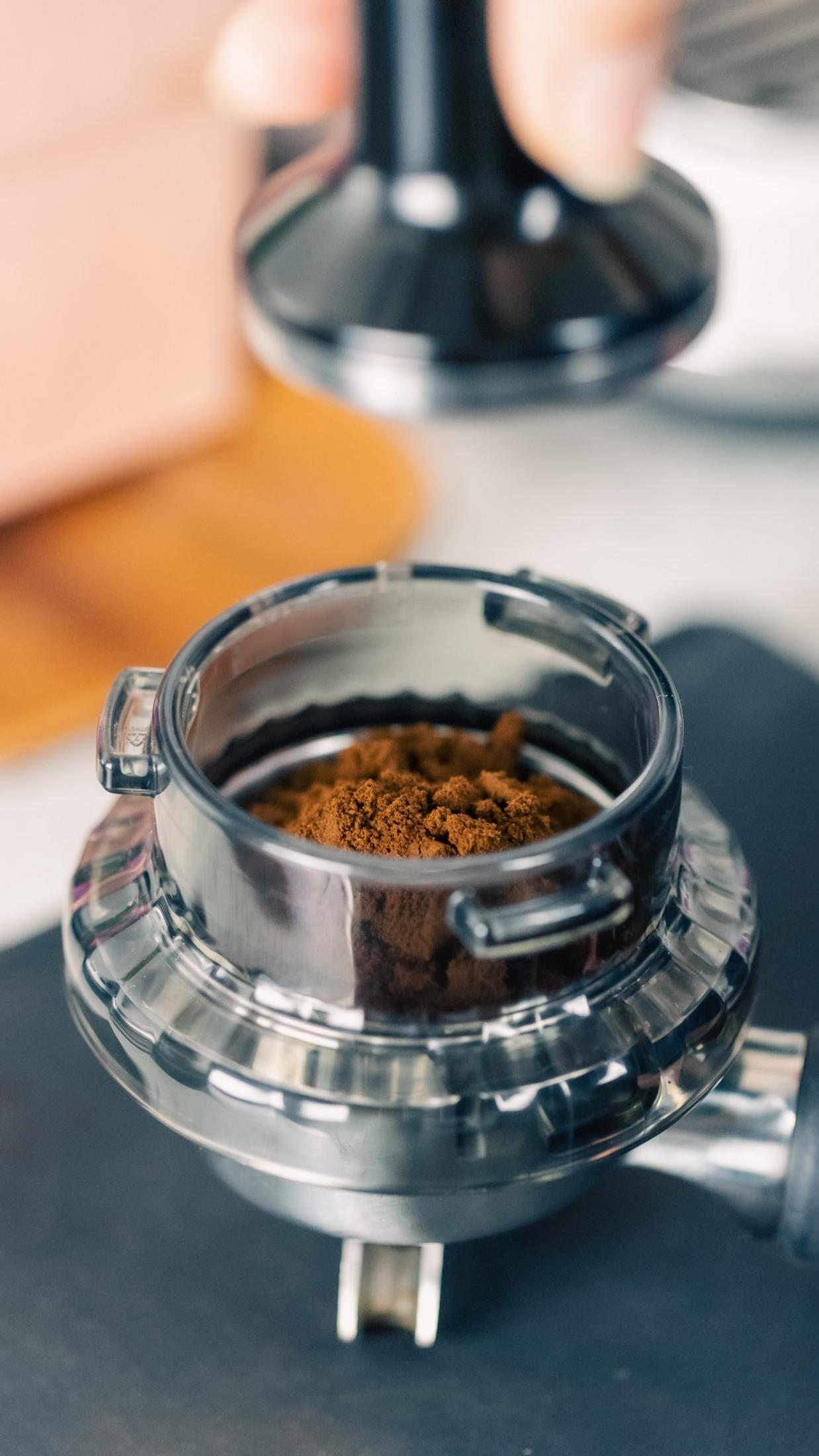 Un tamper presse du café finement moulu dans un panier de porte-filtre. Gros plan.