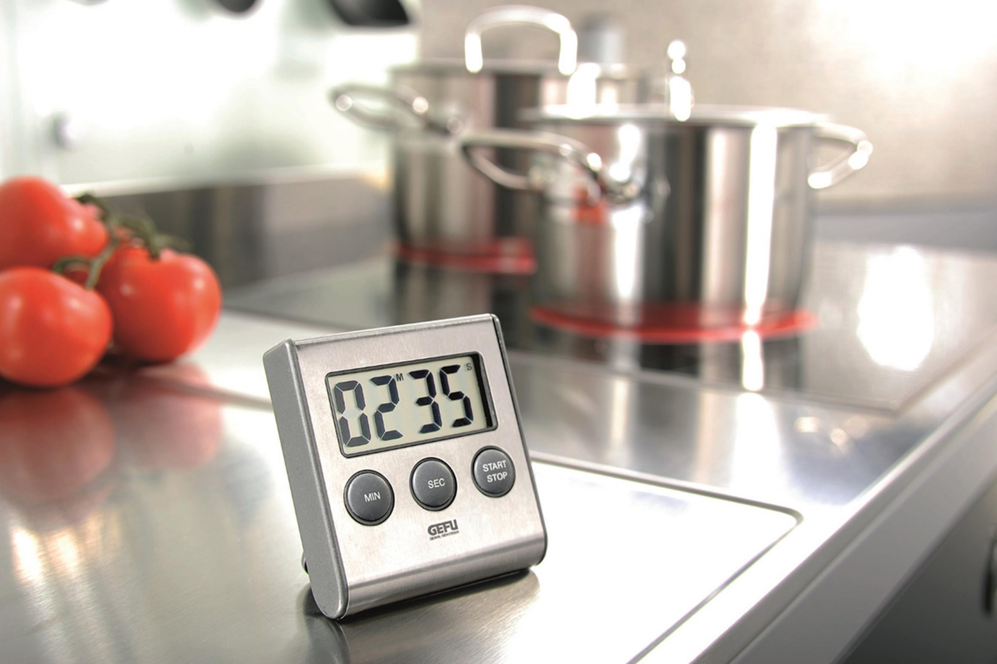 Timer da cucina in acciaio inox con pomodori e pentole sullo sfondo.