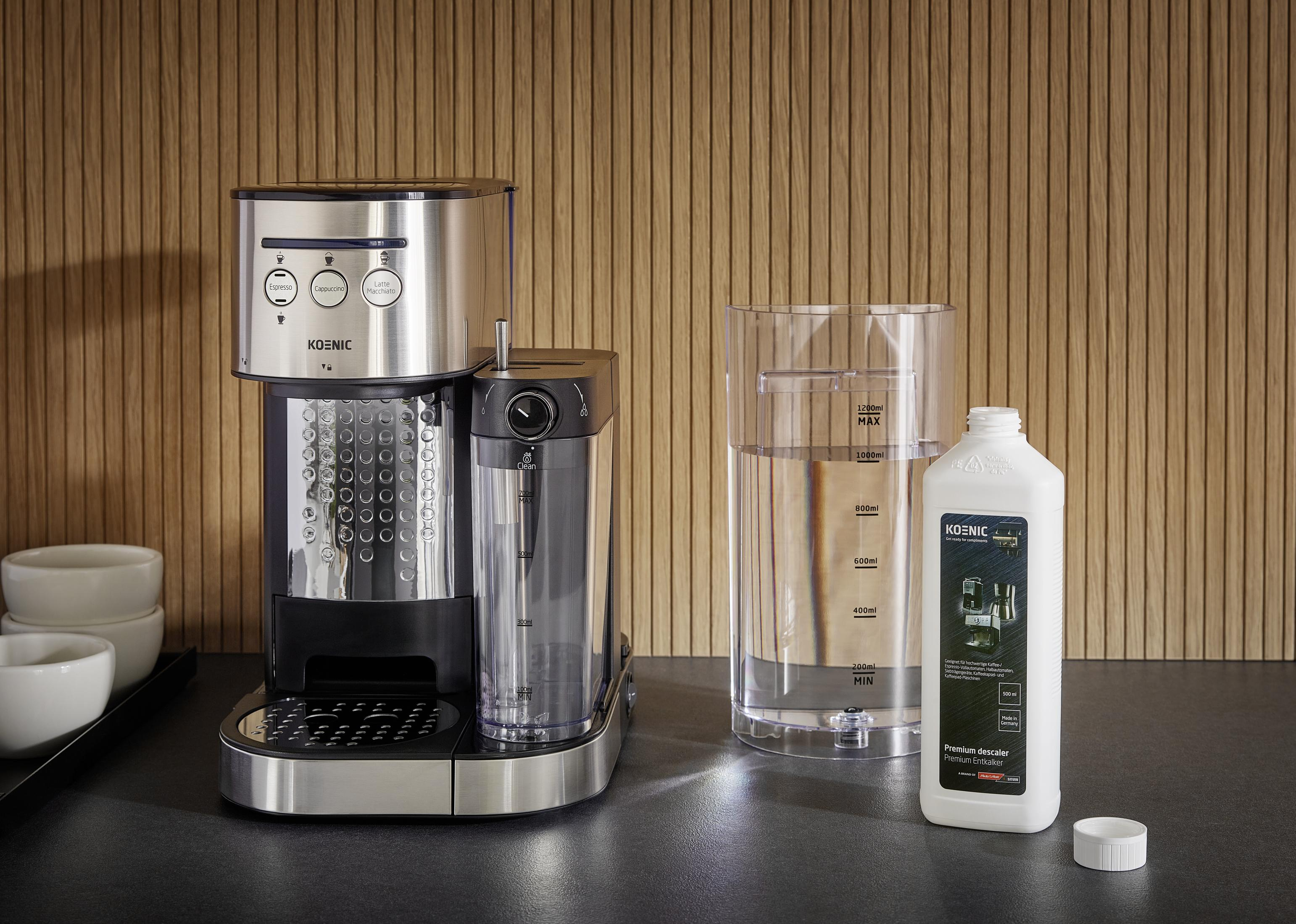 Kaffeemaschine mit Wasserbehälter und Entkalkerflasche auf dunkler Arbeitsfläche.