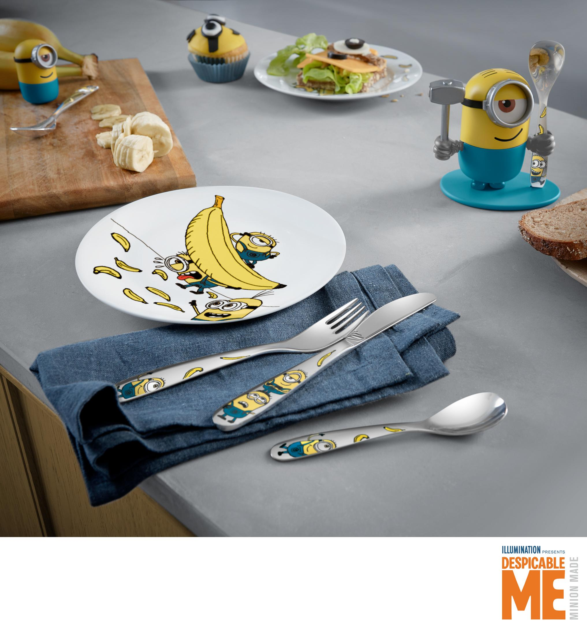 Minion-Geschirr mit Bananen und Beeren. Teller, Besteck auf blauem Tuch.