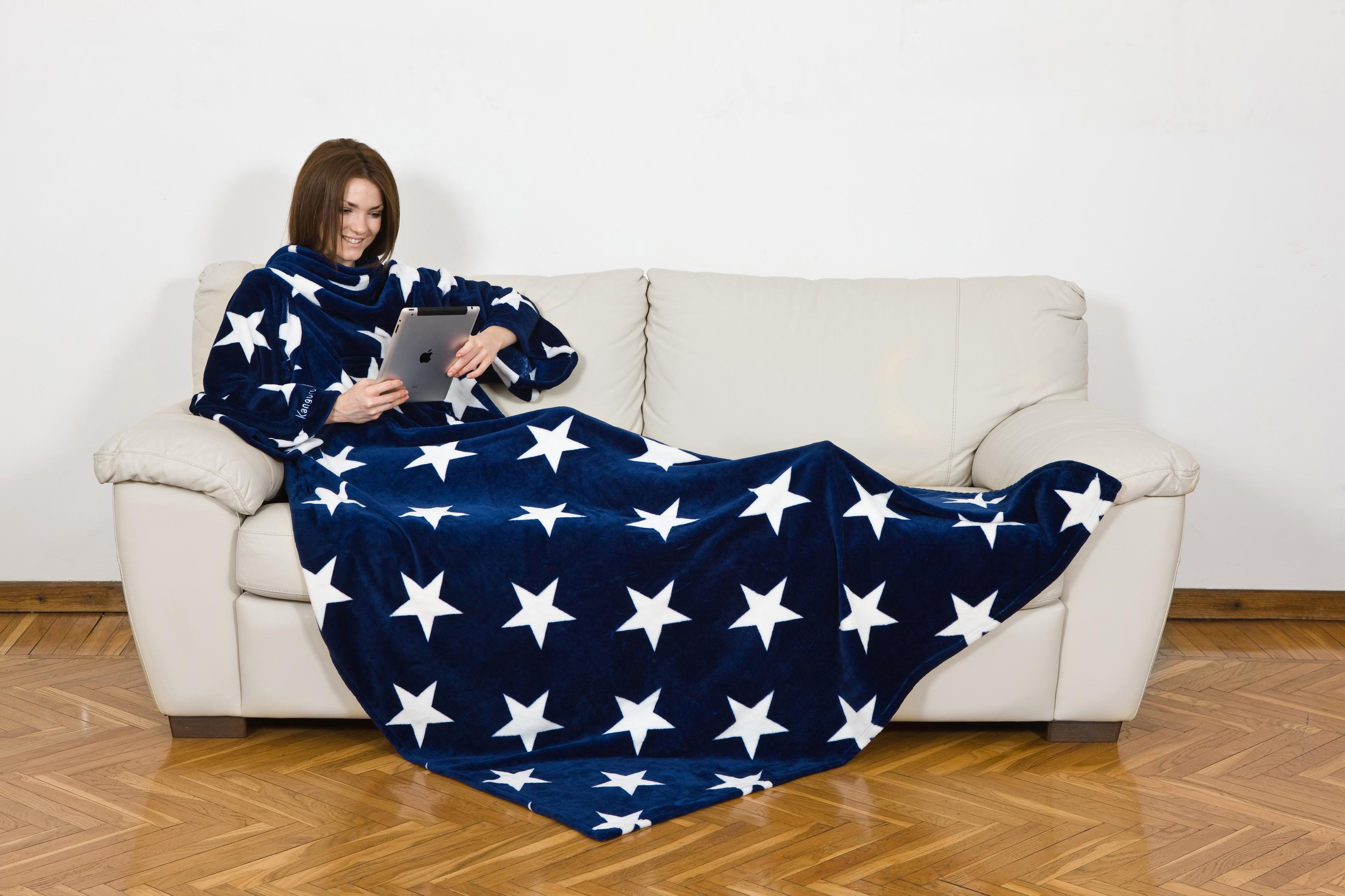 Una donna su un divano avvolta in una coperta a stelle usa un tablet.