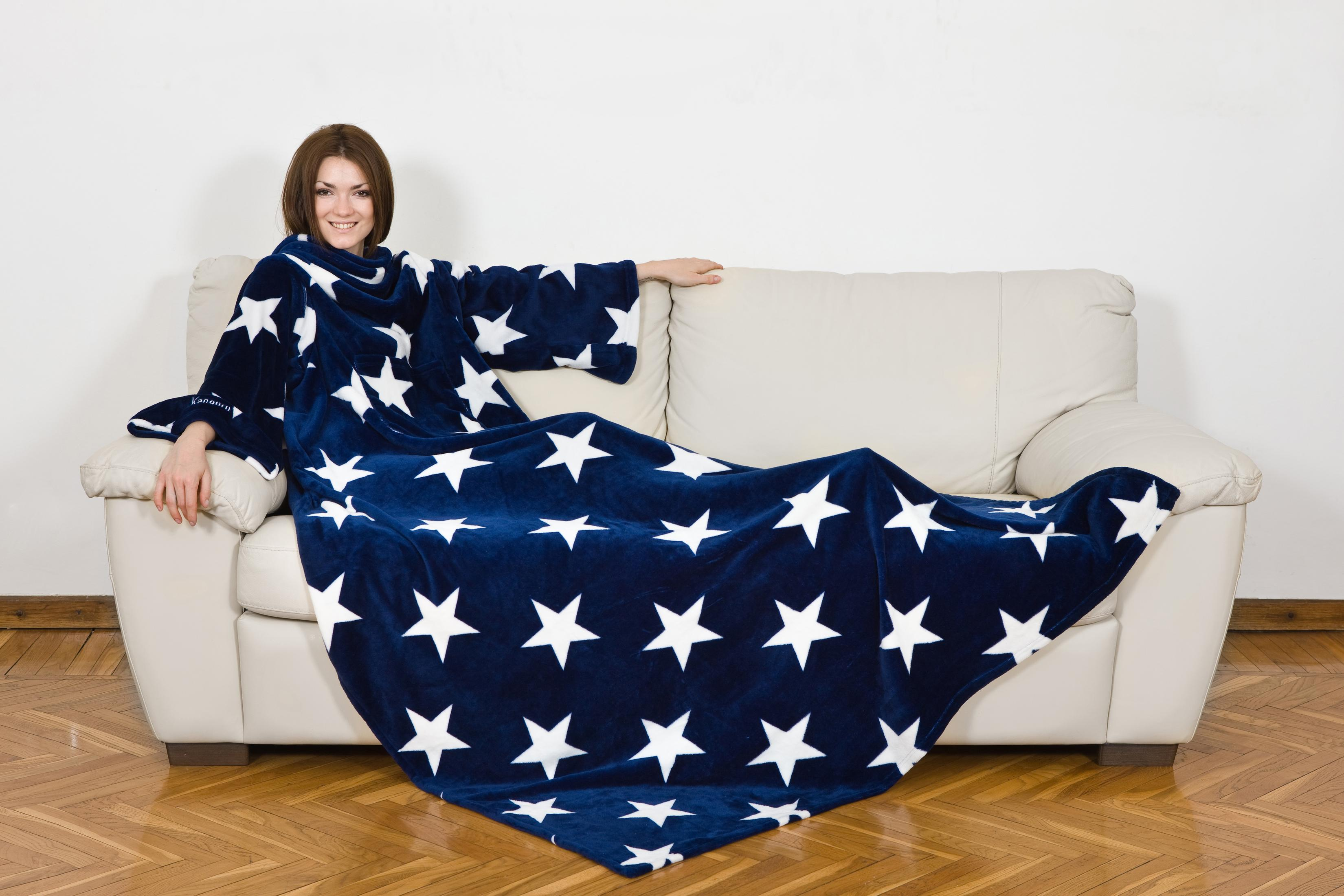 Una donna seduta su un divano, coperta da una coperta blu scuro con stelle bianche.
