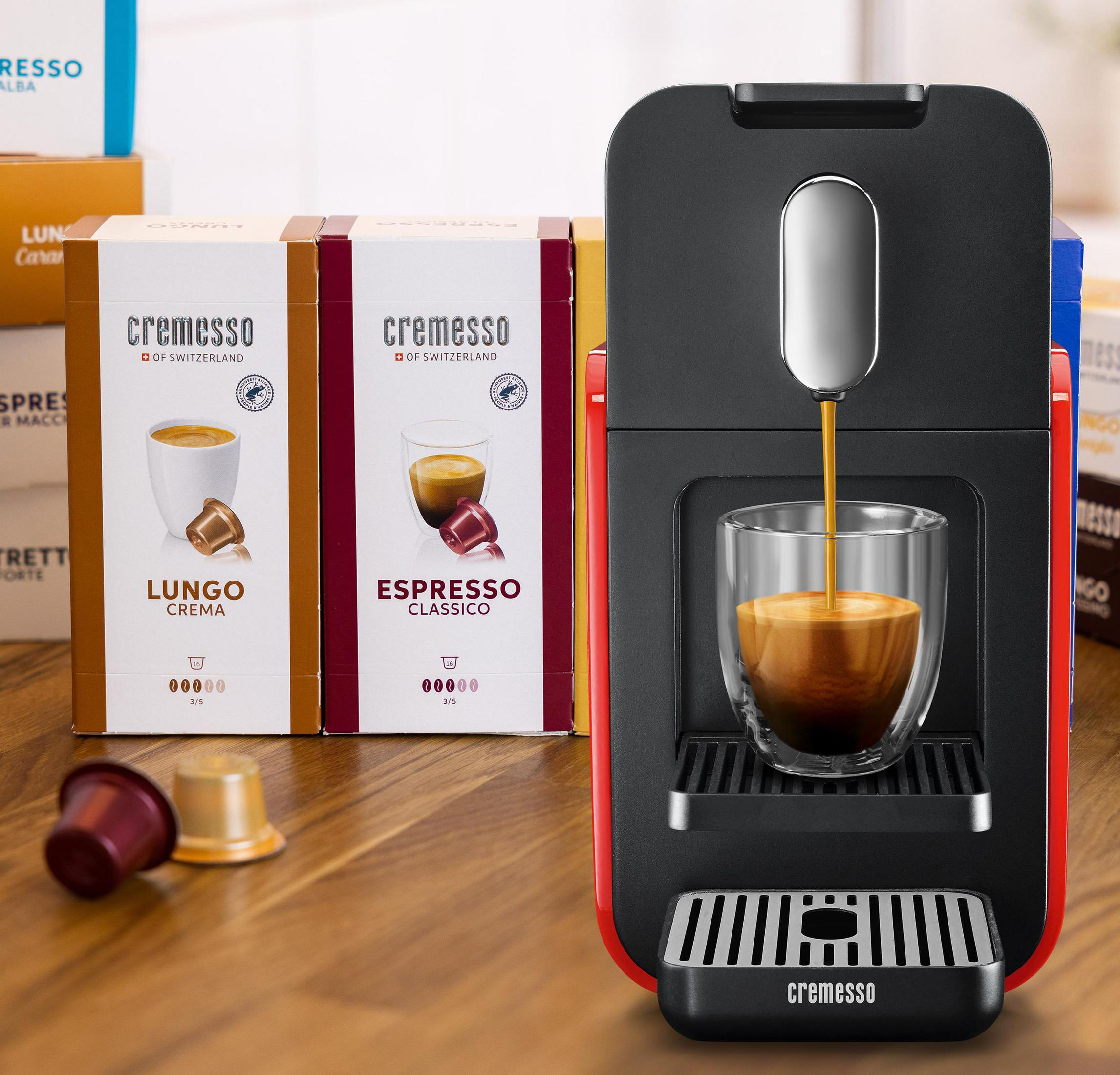 Kaffeemaschine brüht Espresso in ein Glas, daneben Cremesso-Kapselpackungen.