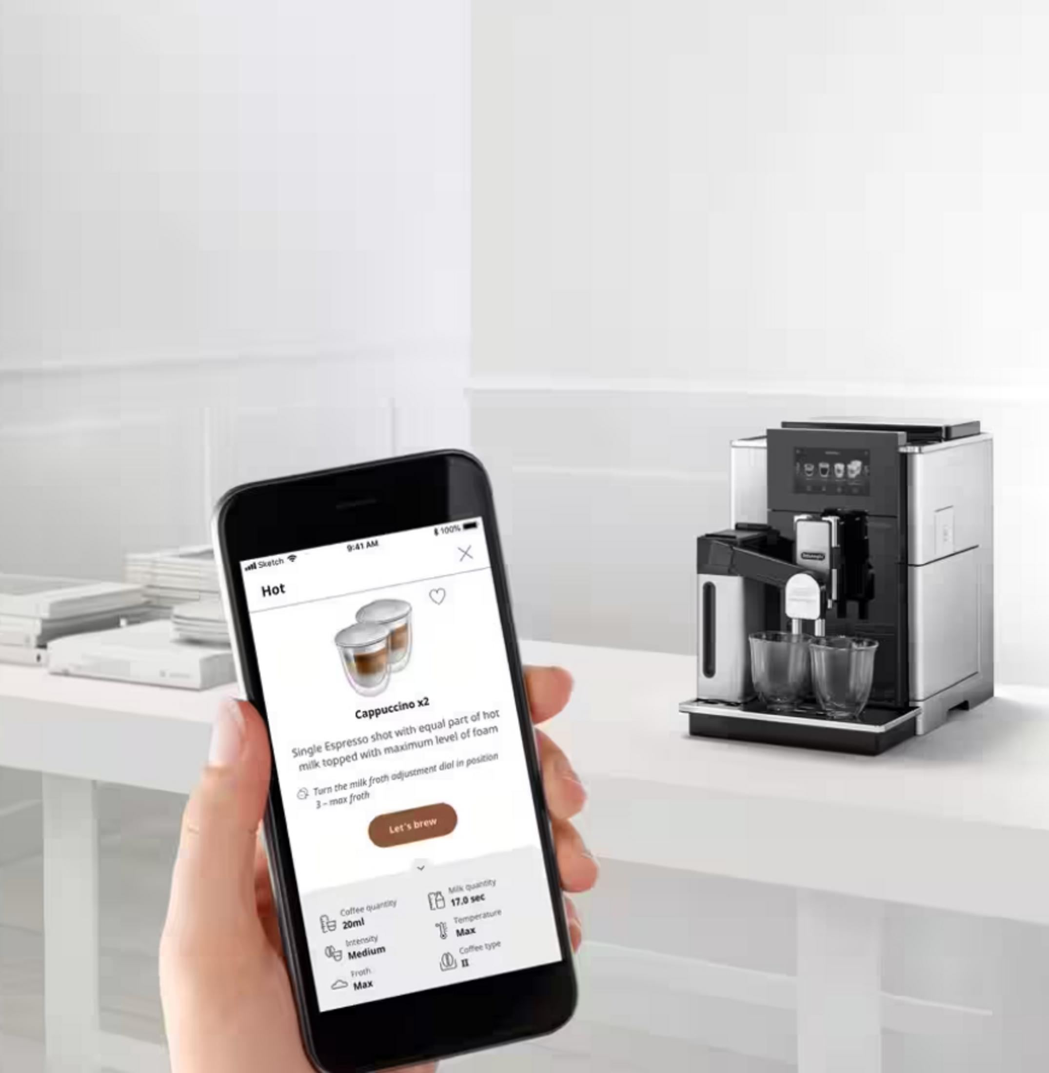 Eine Hand hält ein Smartphone mit einer Kaffee-App. Eine Kaffeemaschine ist in der Nähe.