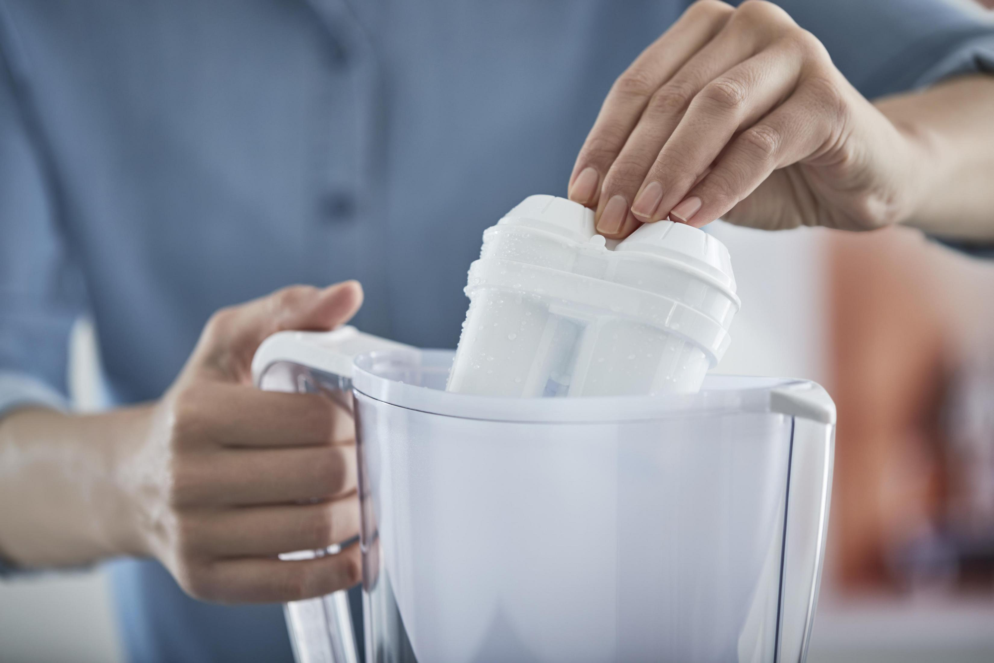 Ręka wkłada biały filtr wody do białego dzbanka.