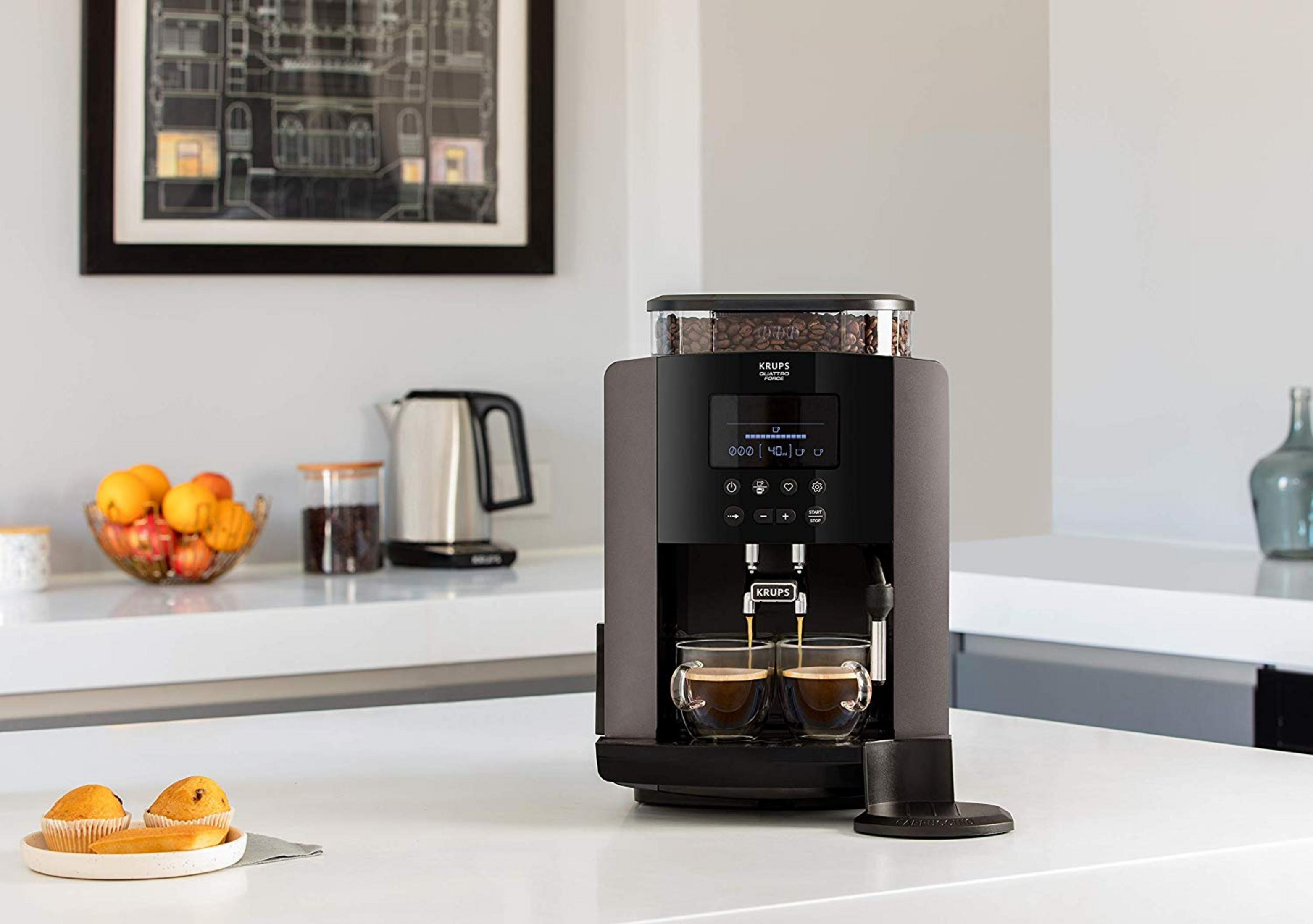 Una macchina da caffè Krups prepara due espressi in tazze trasparenti. I chicchi riempiono il serbatoio superiore.