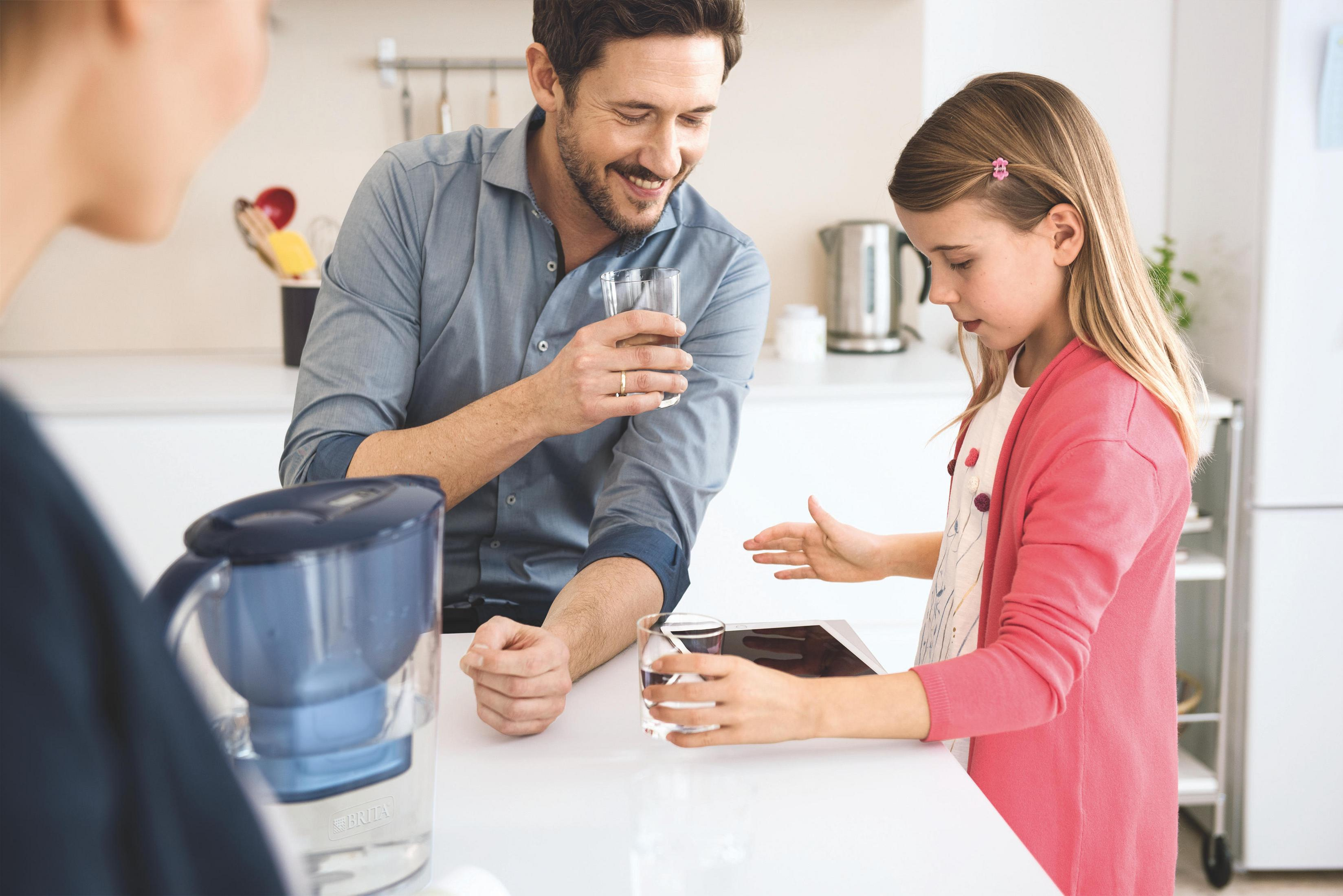 Mann und Mädchen trinken Wasser in der Küche neben einem Wasserfilter.