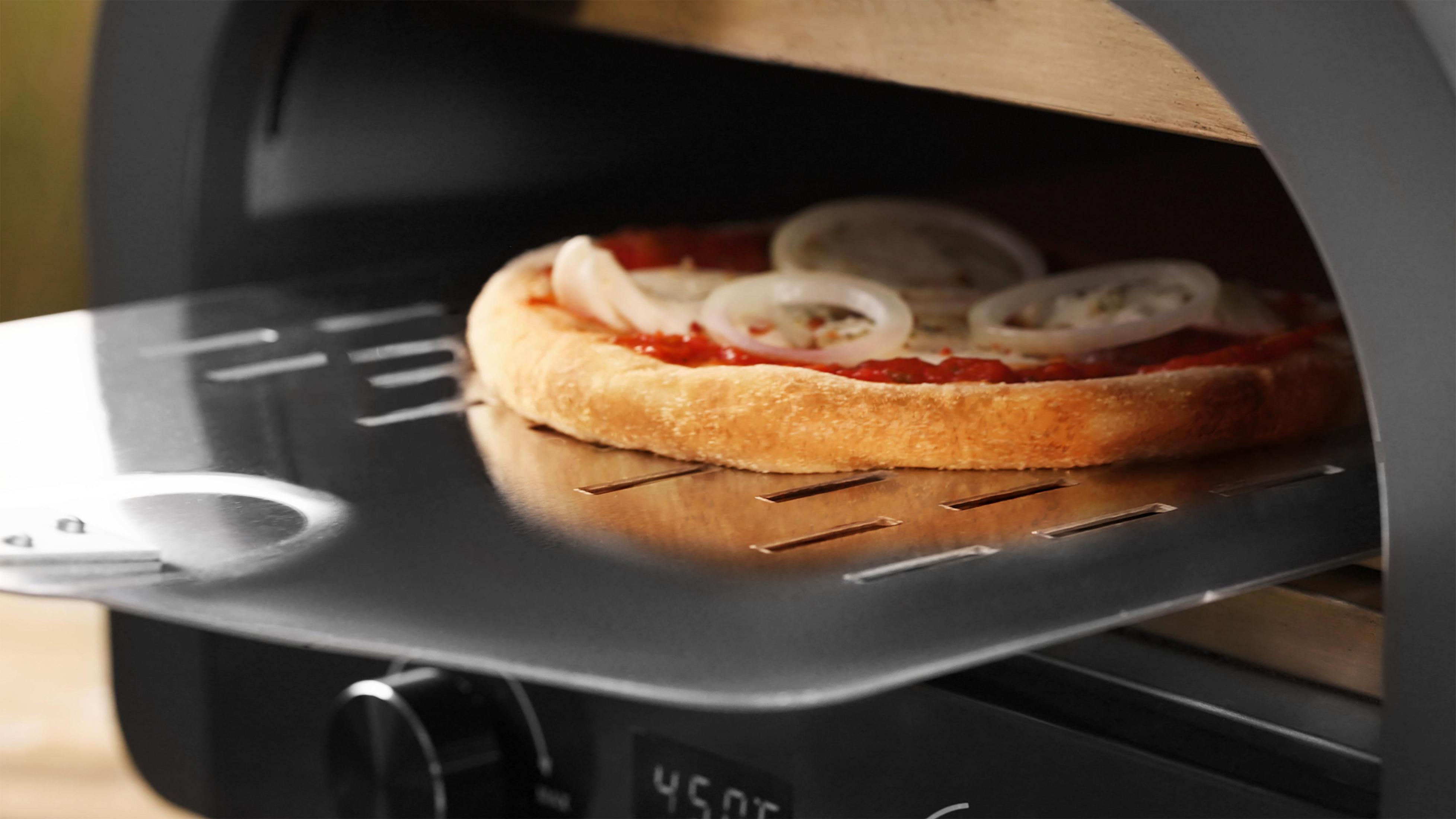 Eine ungebackene Pizza mit Zwiebeln wird aus einem Ofen geschoben.