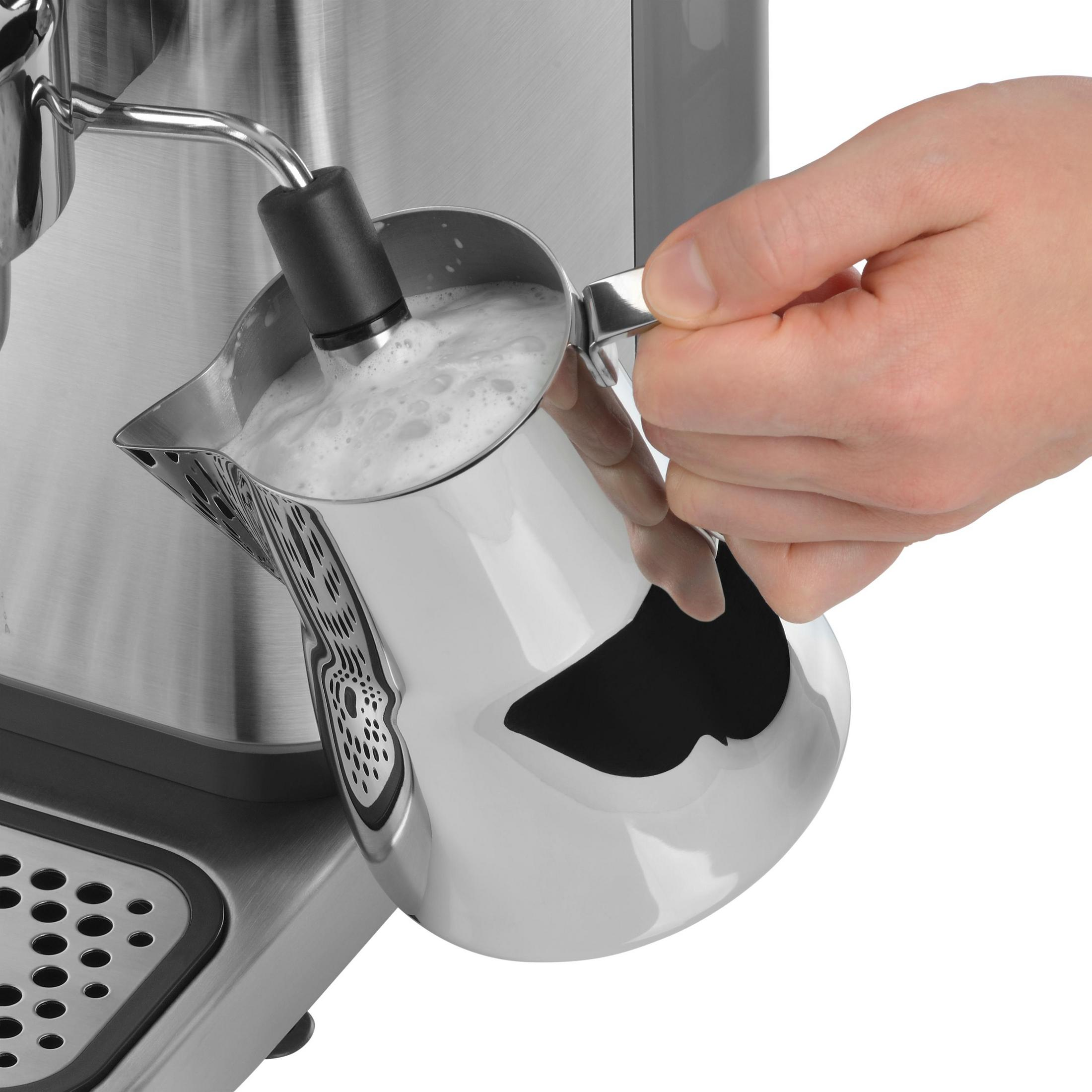 Person schäumt Milch in einem Metallkrug mit einer Kaffeemaschine.